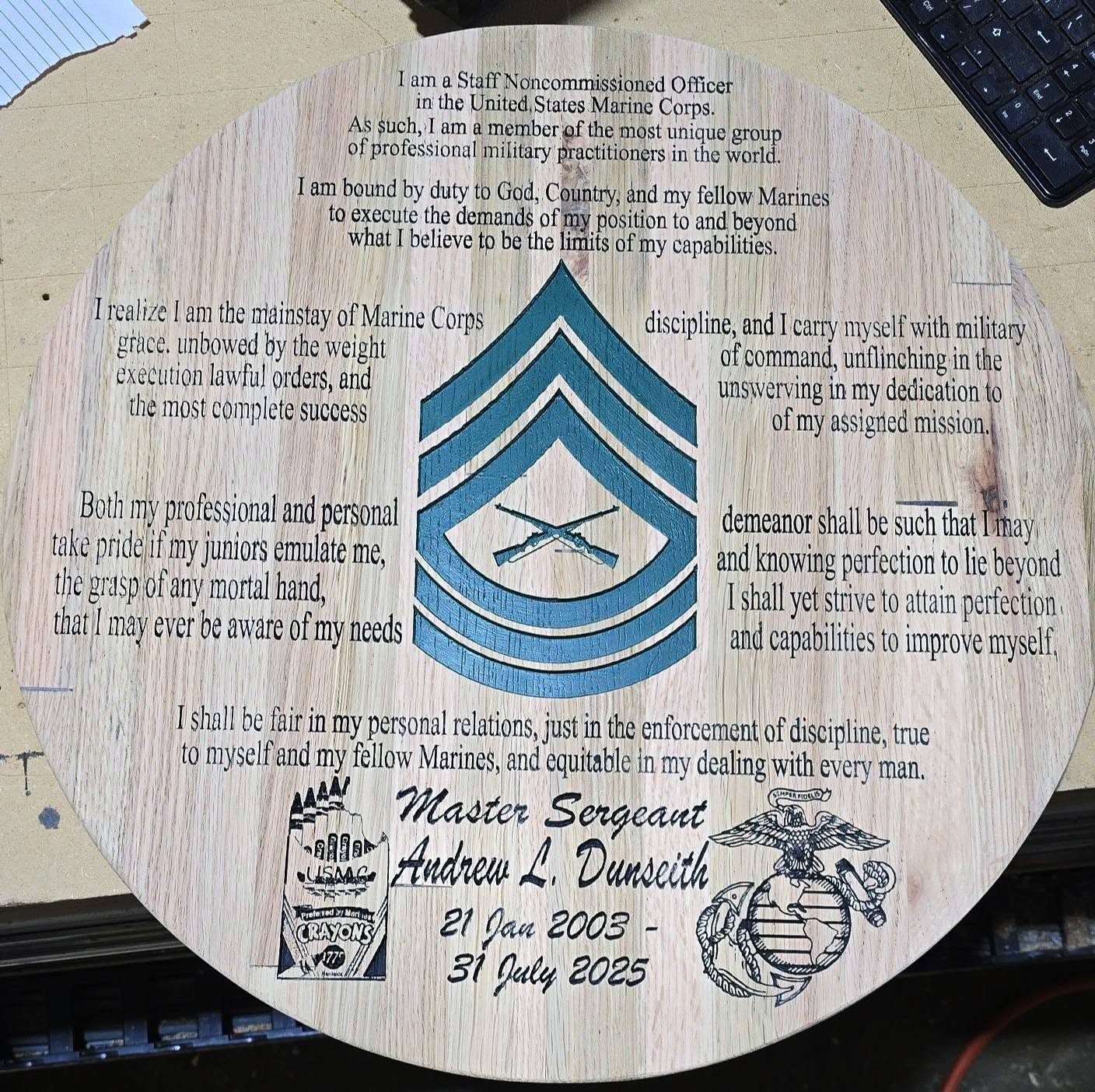 Round wood panel engraved with the Marine Corps staff noncommissioned officer creed, a rank emblem, and Master Sergeant Andrew L. Dunseith’s name and service dates.