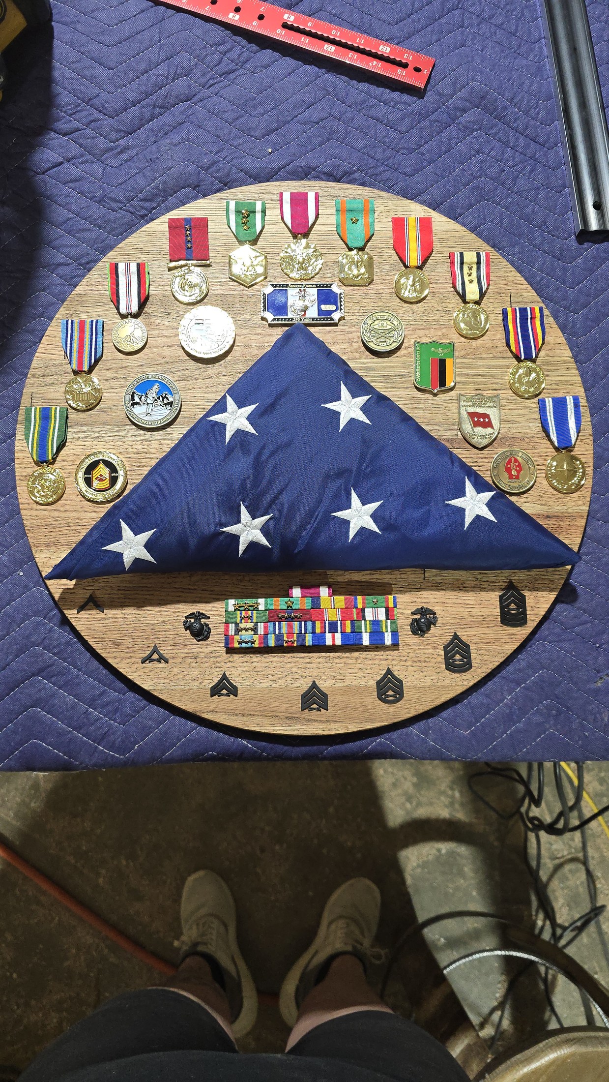Military medals, ribbons and Marine Corps insignia arranged around a folded American flag on a round wooden display.