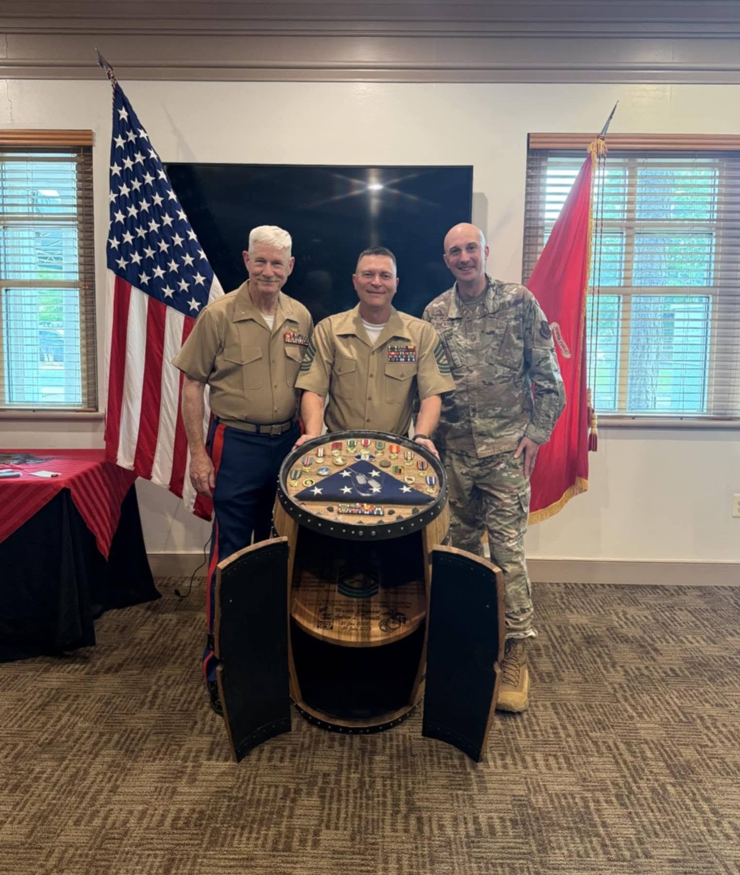 Retiring Marine Master Sergeant Andy Dunseith stands between two fellow service members behind his open barrel display cabinet.