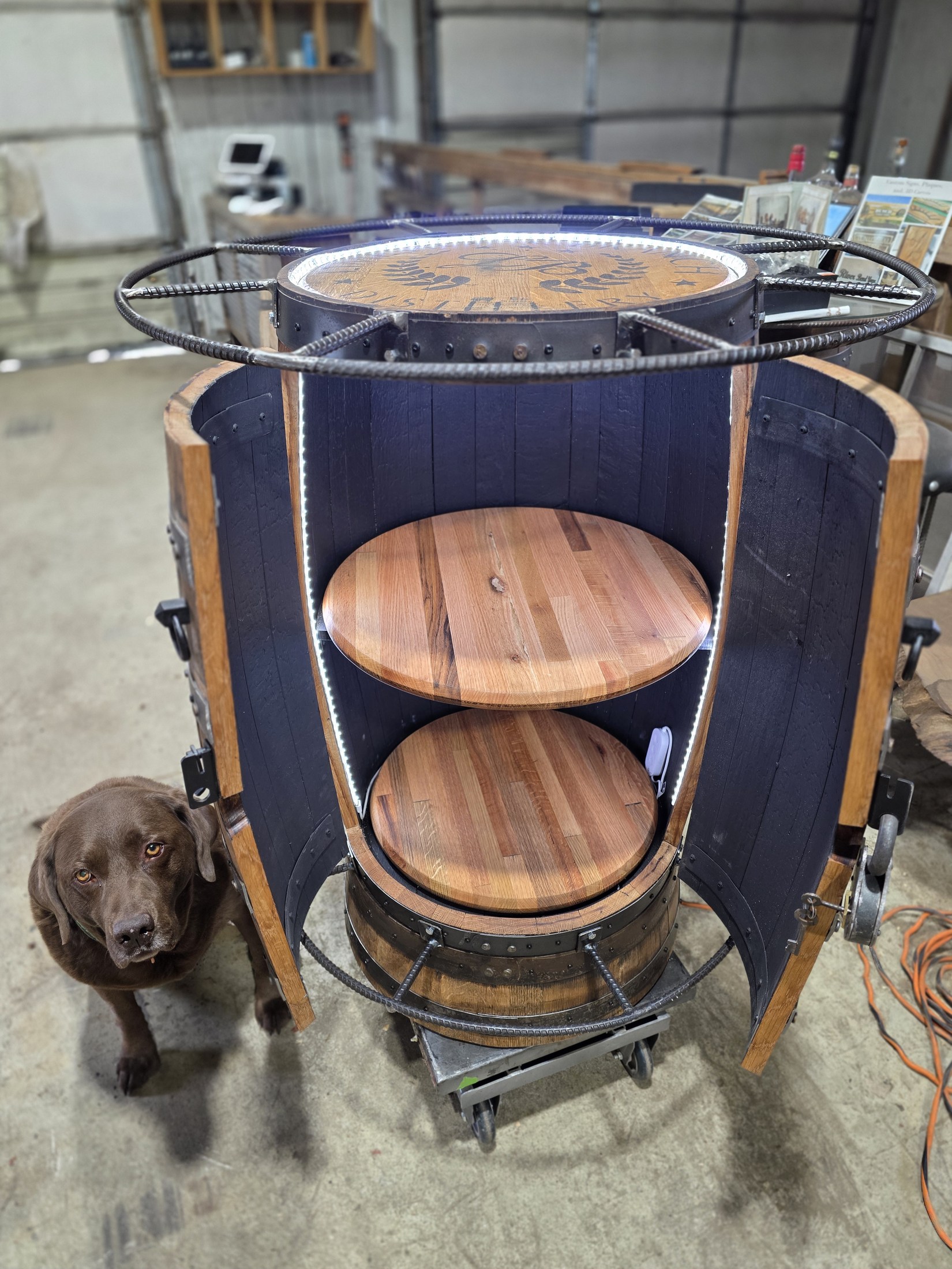 Open barrel cabinet with two circular wood shelves, dark interior panels and doors swung to both sides.