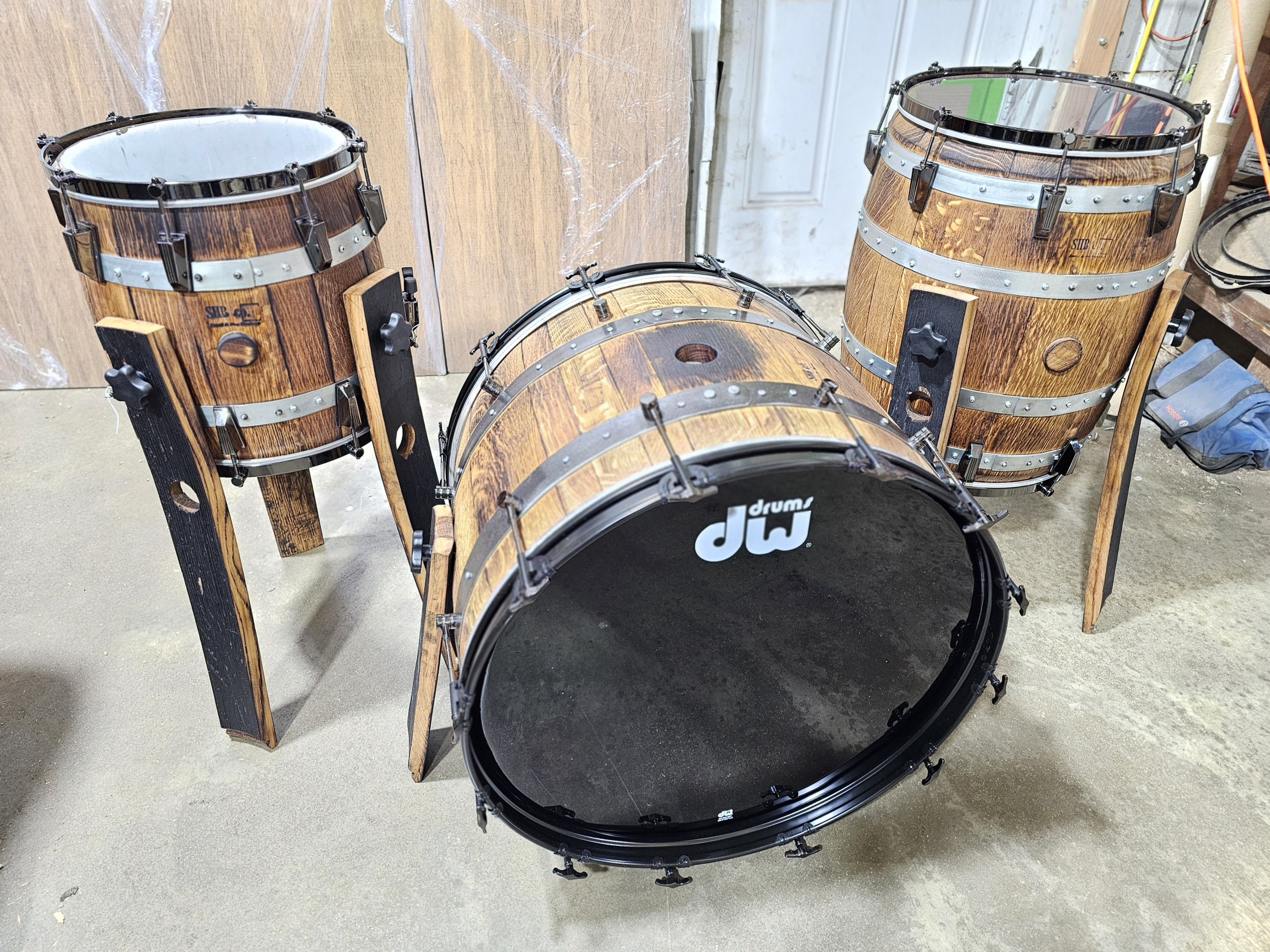 Three-piece barrel drum kit with black heads, tension rods, metal hoops and tall wooden supports.