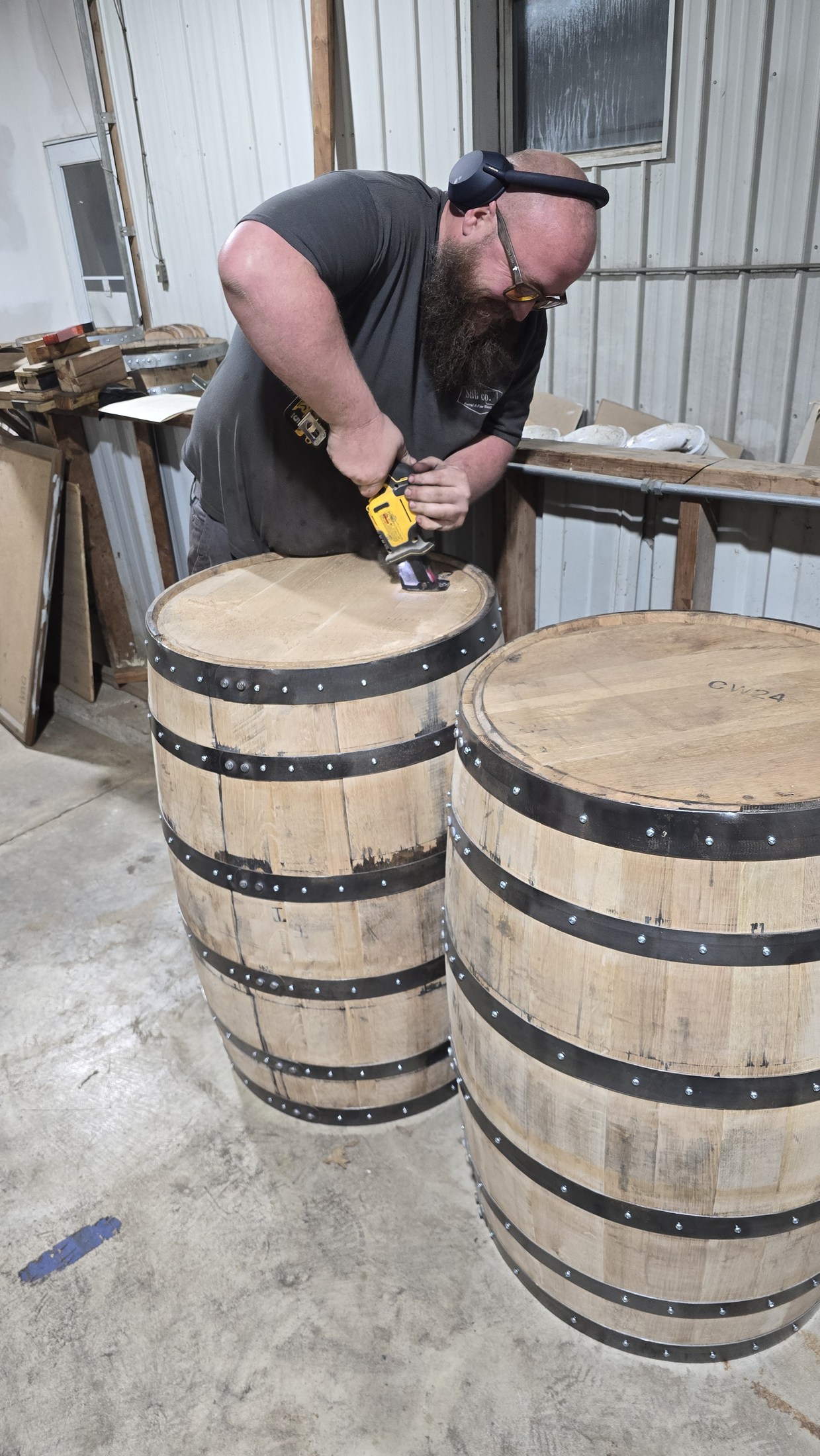 Ryan works on the end of a barrel beside another barrel during drum construction.
