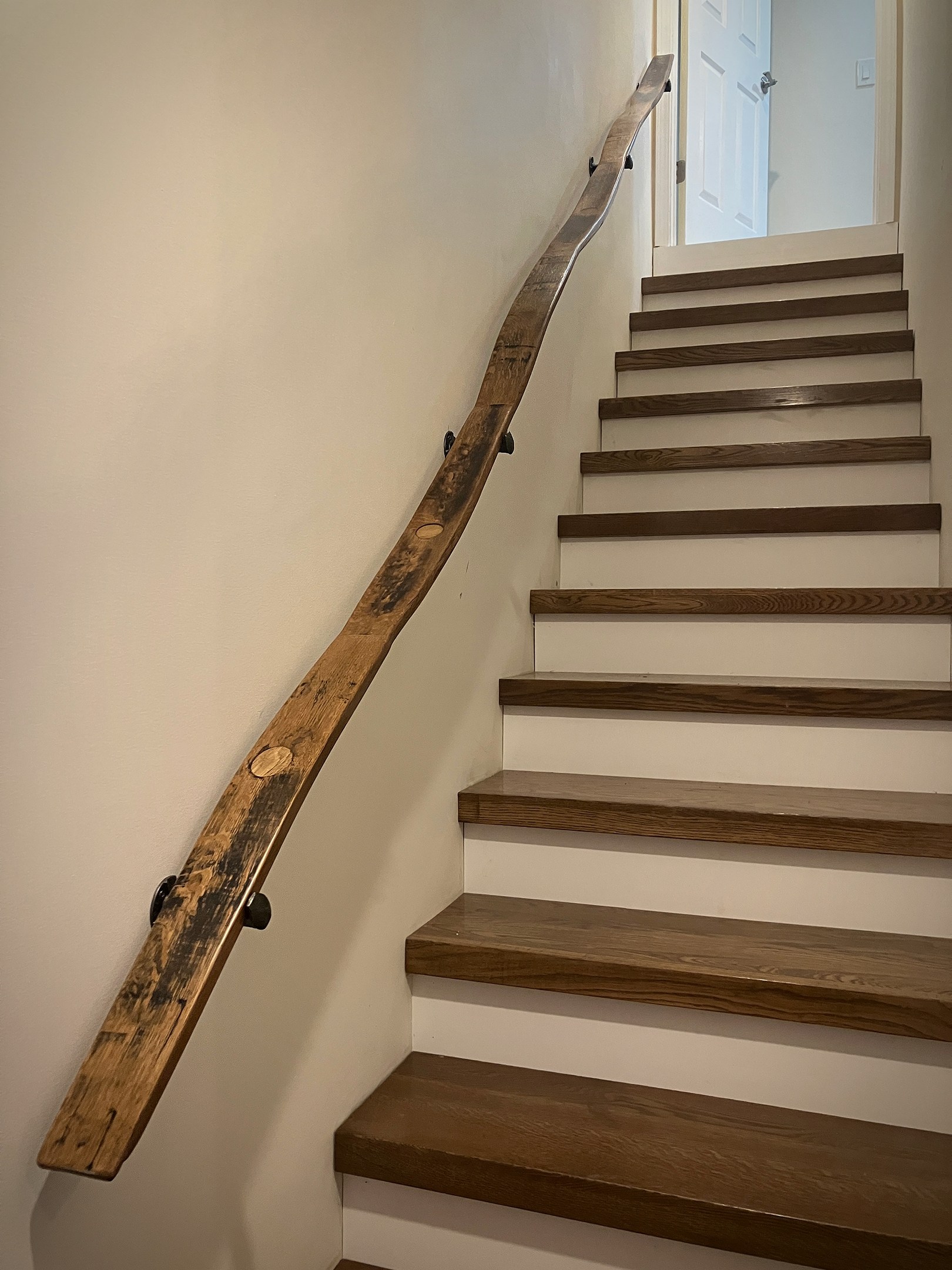 A long barrel-stave handrail follows the slope of an indoor staircase on dark wall brackets.