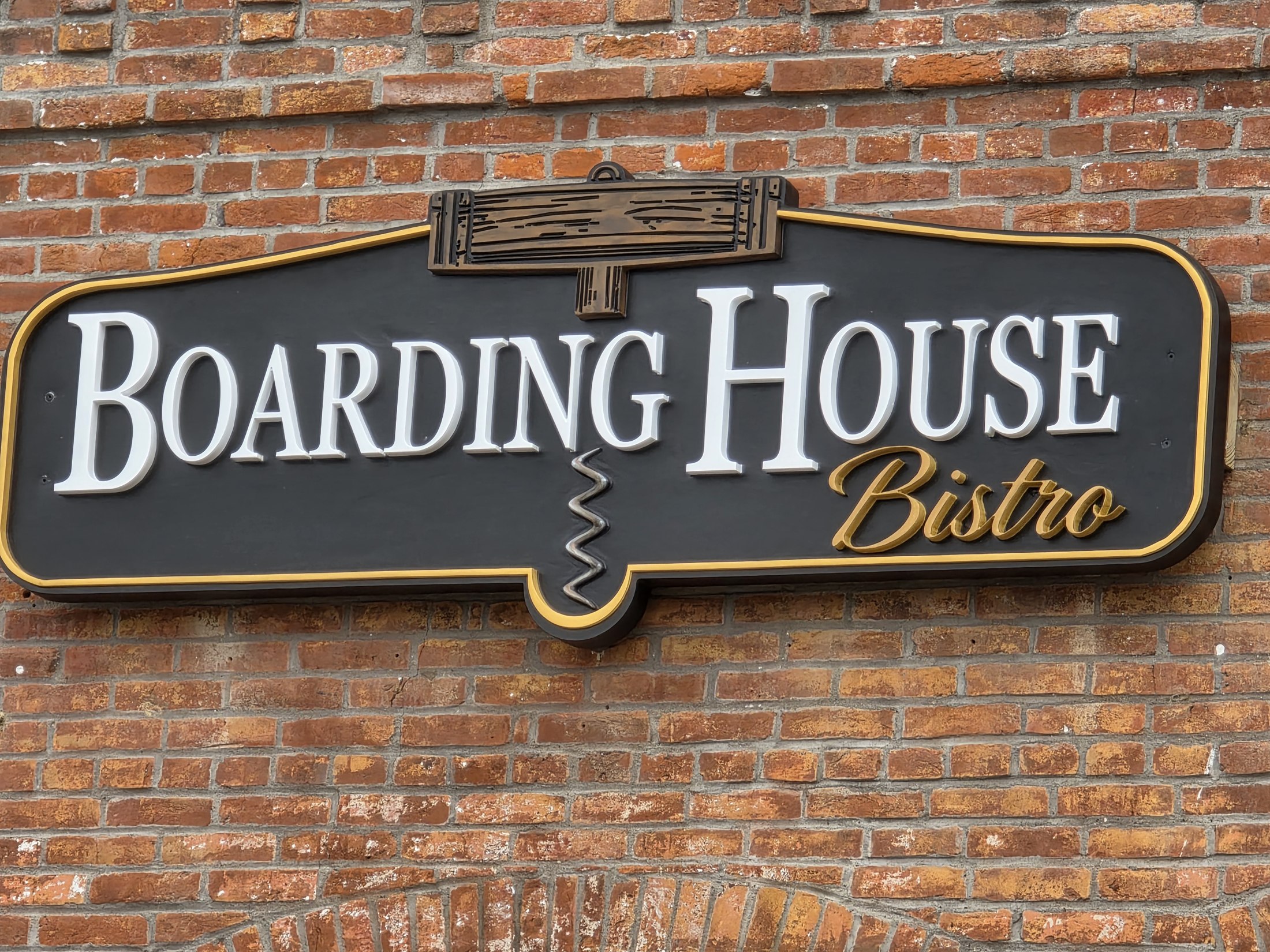 Black, white and gold Boarding House Bistro dimensional sign mounted on a brick facade.