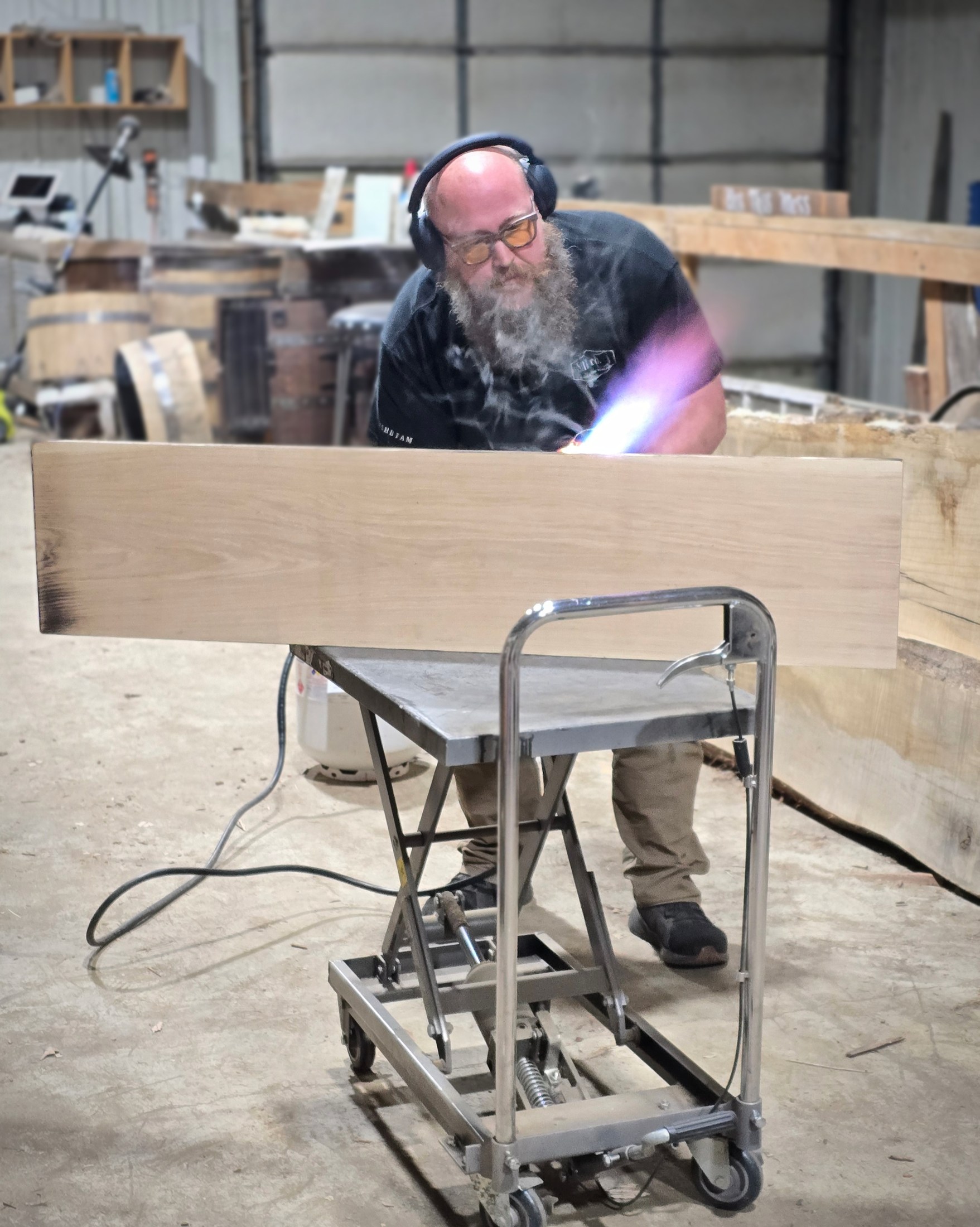 Ryan hand-charring a long wooden waypoint sign with a torch in the SHB workshop.