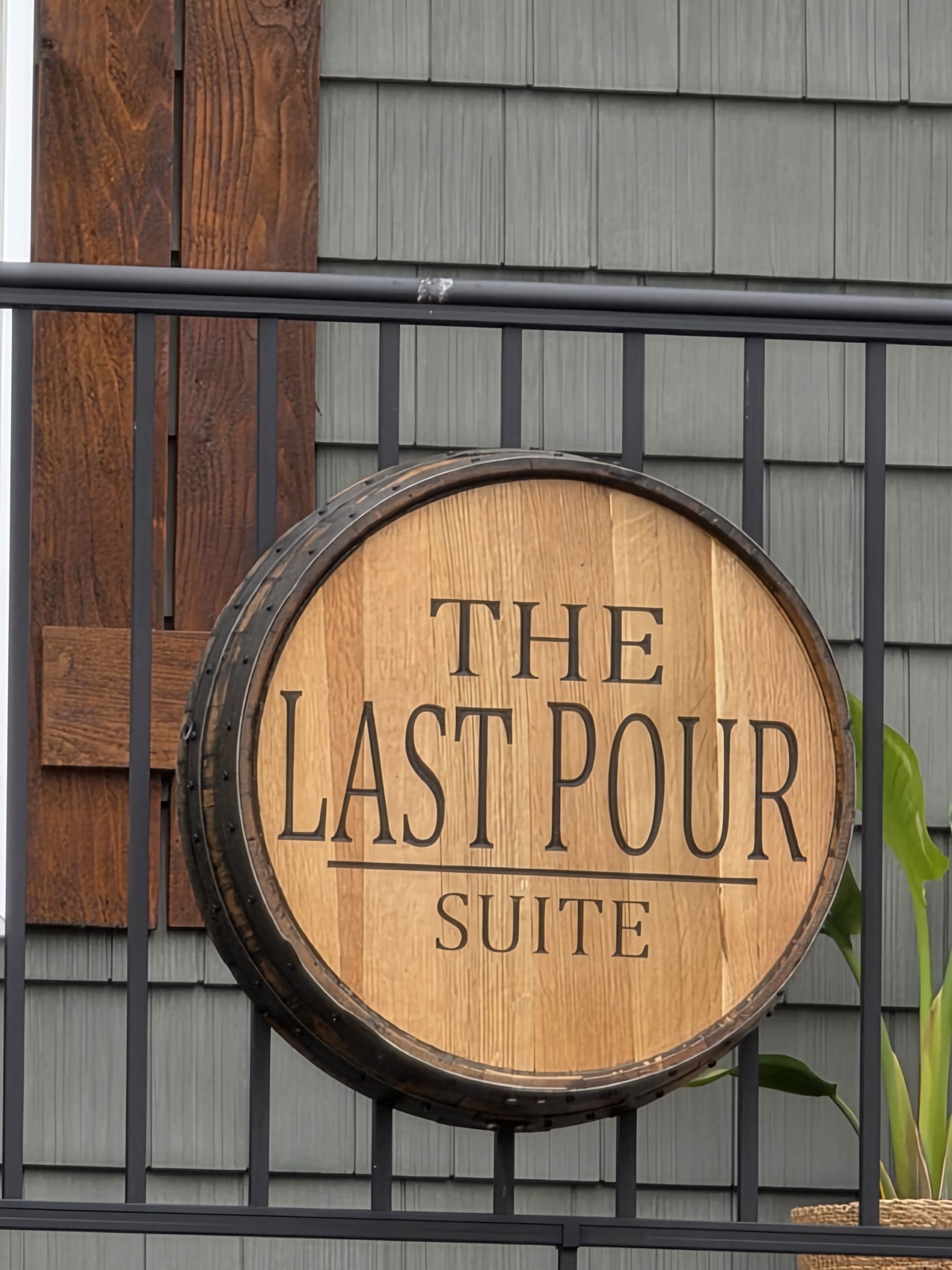 Round wooden The Last Pour Suite sign attached to a black railing.