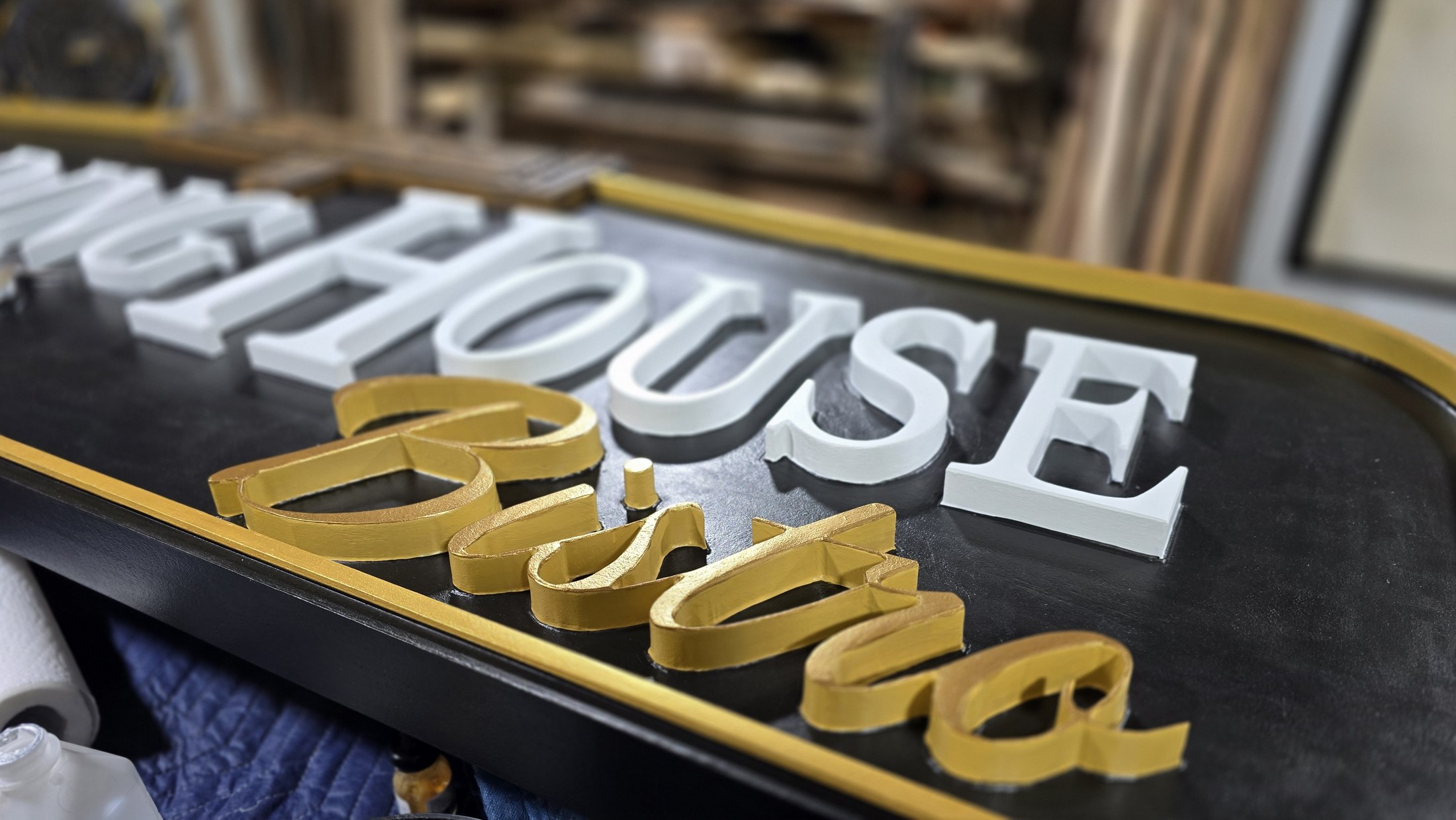 Low-angle close-up of raised white and gold Boarding House Bistro lettering against a dark sign face.