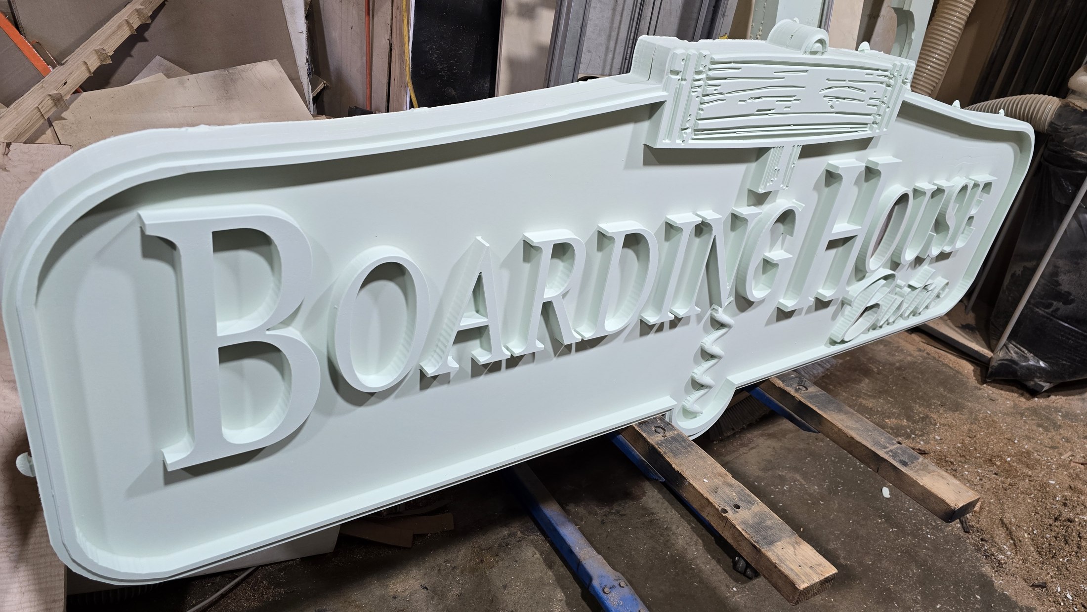 The large Boarding House Bistro sign lying in the shop with a light primed surface and dimensional lettering.