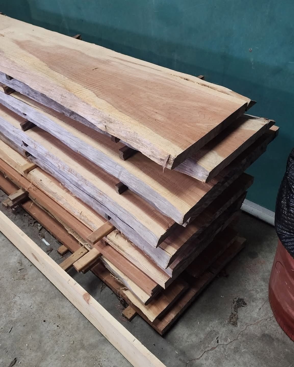 Stack of wide cedar boards with pale edges and warm pink and brown grain in the workshop.