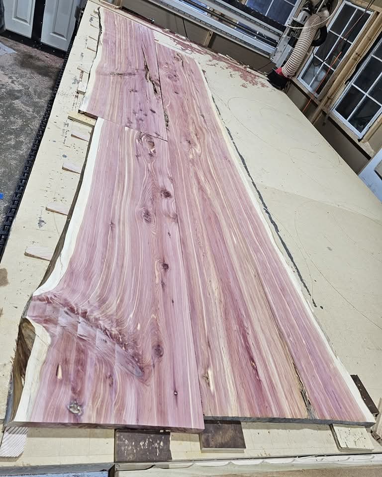 Two long cedar boards on the CNC bed during surfacing, showing pink heartwood and pale sapwood.