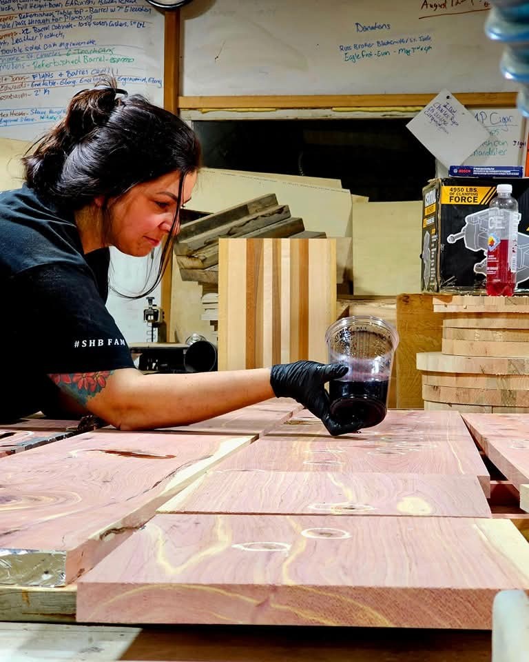 Faith wearing gloves while working on knots in cedar boards laid across the workshop bench.