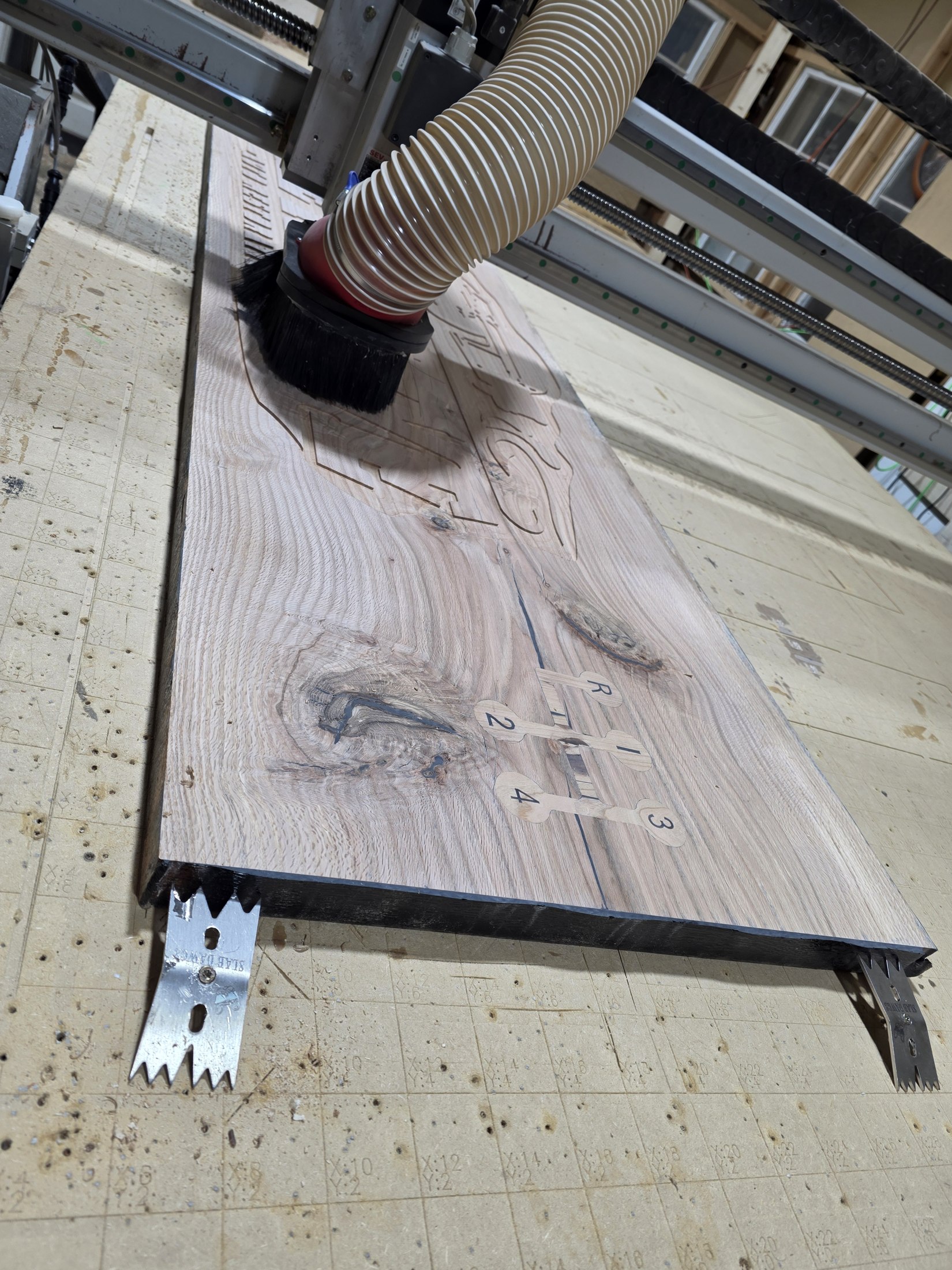 A long wooden panel positioned beneath the CNC router in the workshop.