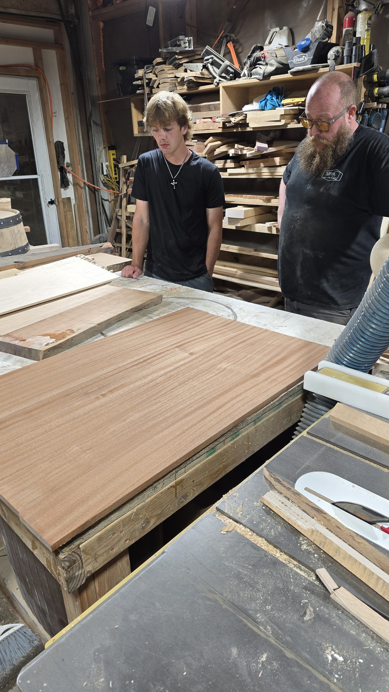 Ben and Ryan beside wood panels and clamps laid out on the workshop bench.