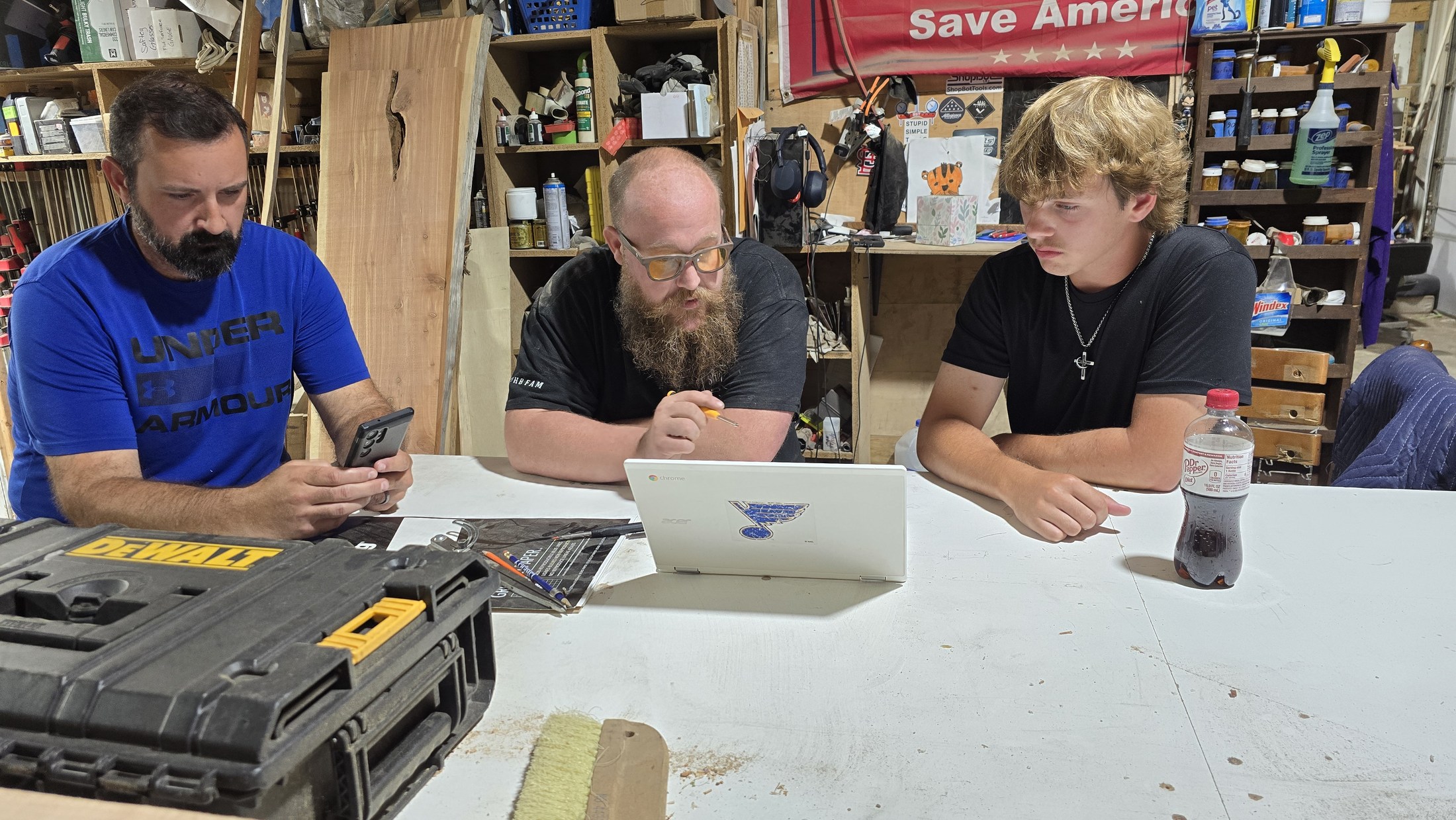 Ben, Ryan and another adult gather around a laptop and notes at a workshop table during the flag-retirement project.