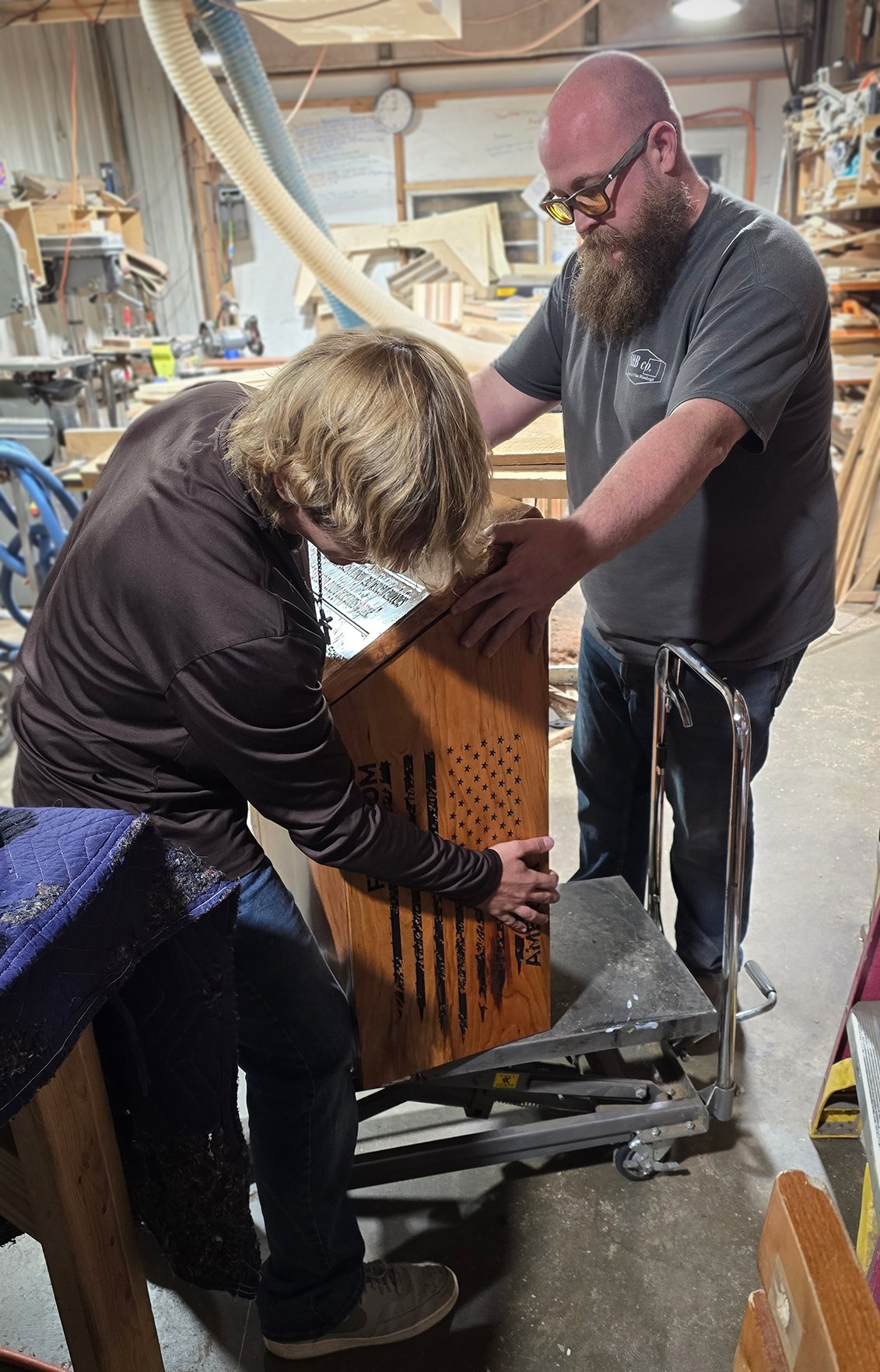Two people working together around the wooden flag-retirement box in the shop.