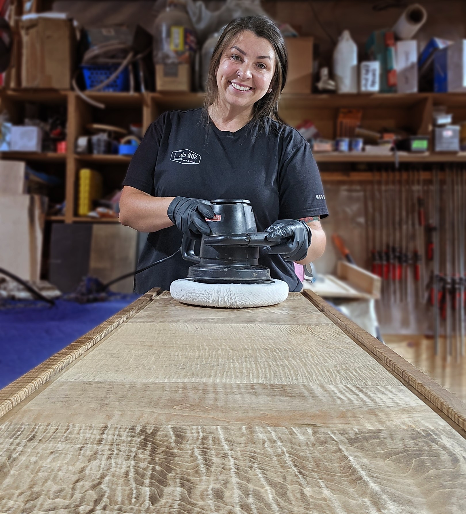 Faith using a powered finishing tool on a long figured wood surface in the SHB workshop.