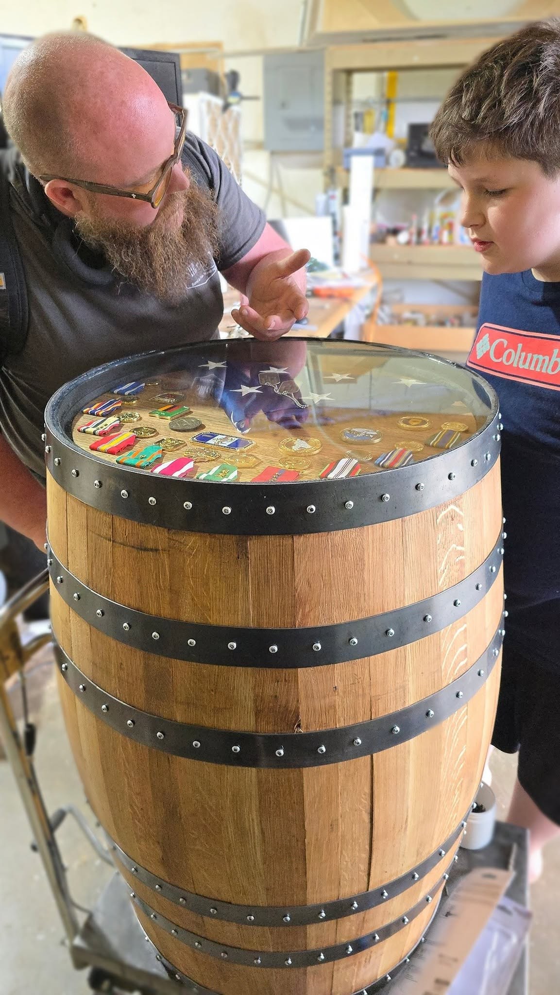 Ryan points out details in a military shadow-box barrel cabinet while Ben looks through the glass top.