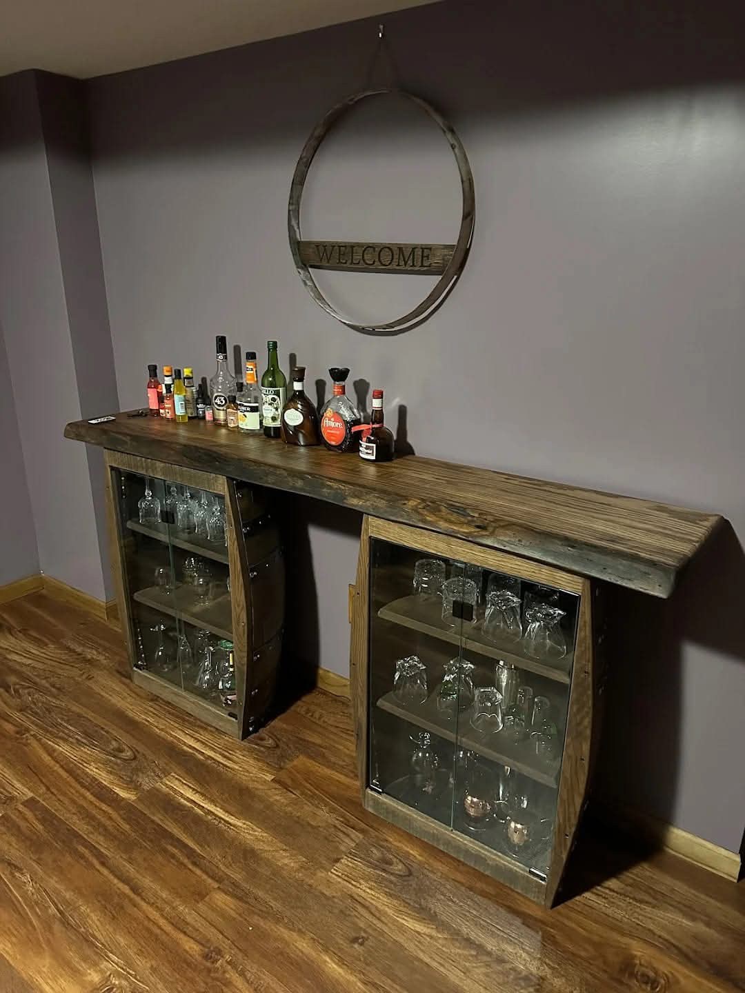 A white-oak live-edge slab spans two half-barrel cabinets with glass doors in a customer’s home.