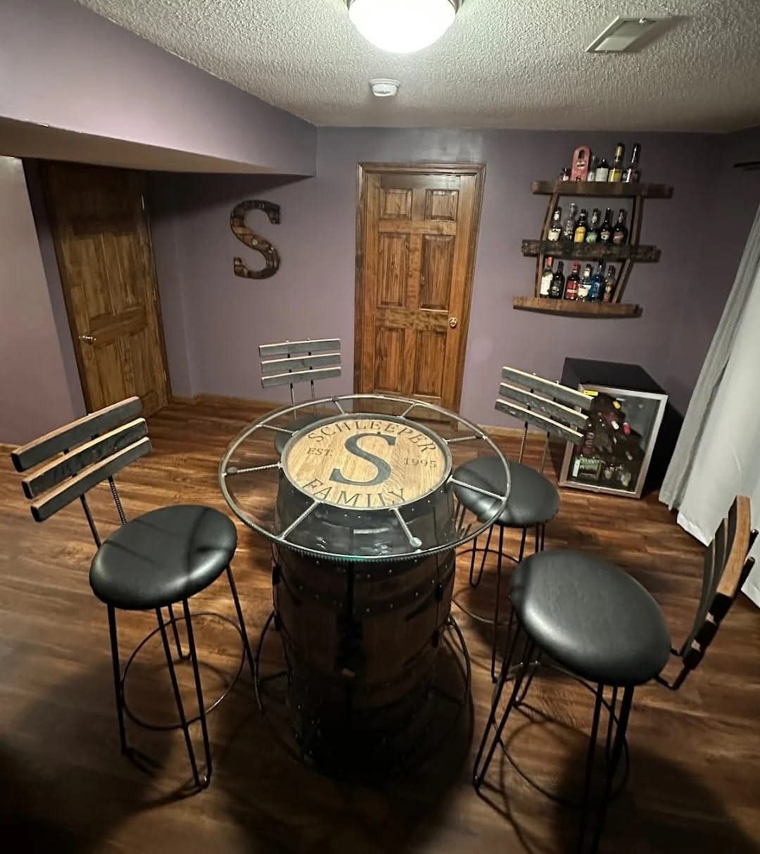 A personalized glass-top barrel cocktail table and stave-back stools arranged in a furnished home.