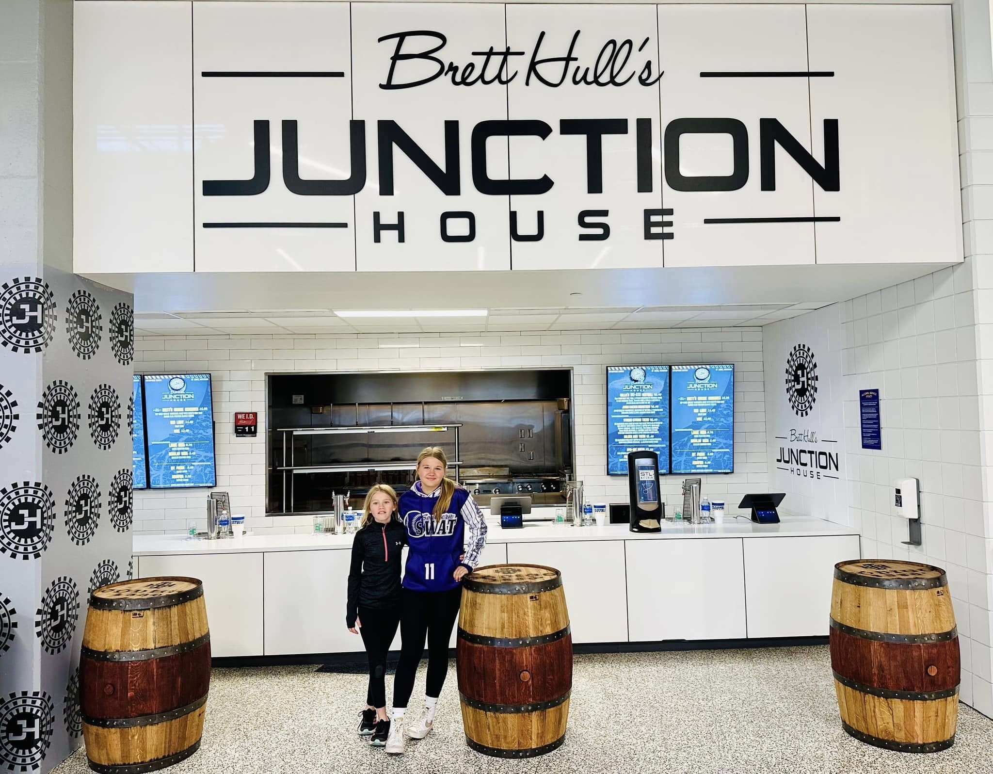 Three SHB-made barrel displays in front of Brett Hull’s Junction House concession at Enterprise Center, with two visitors beside the middle barrel.