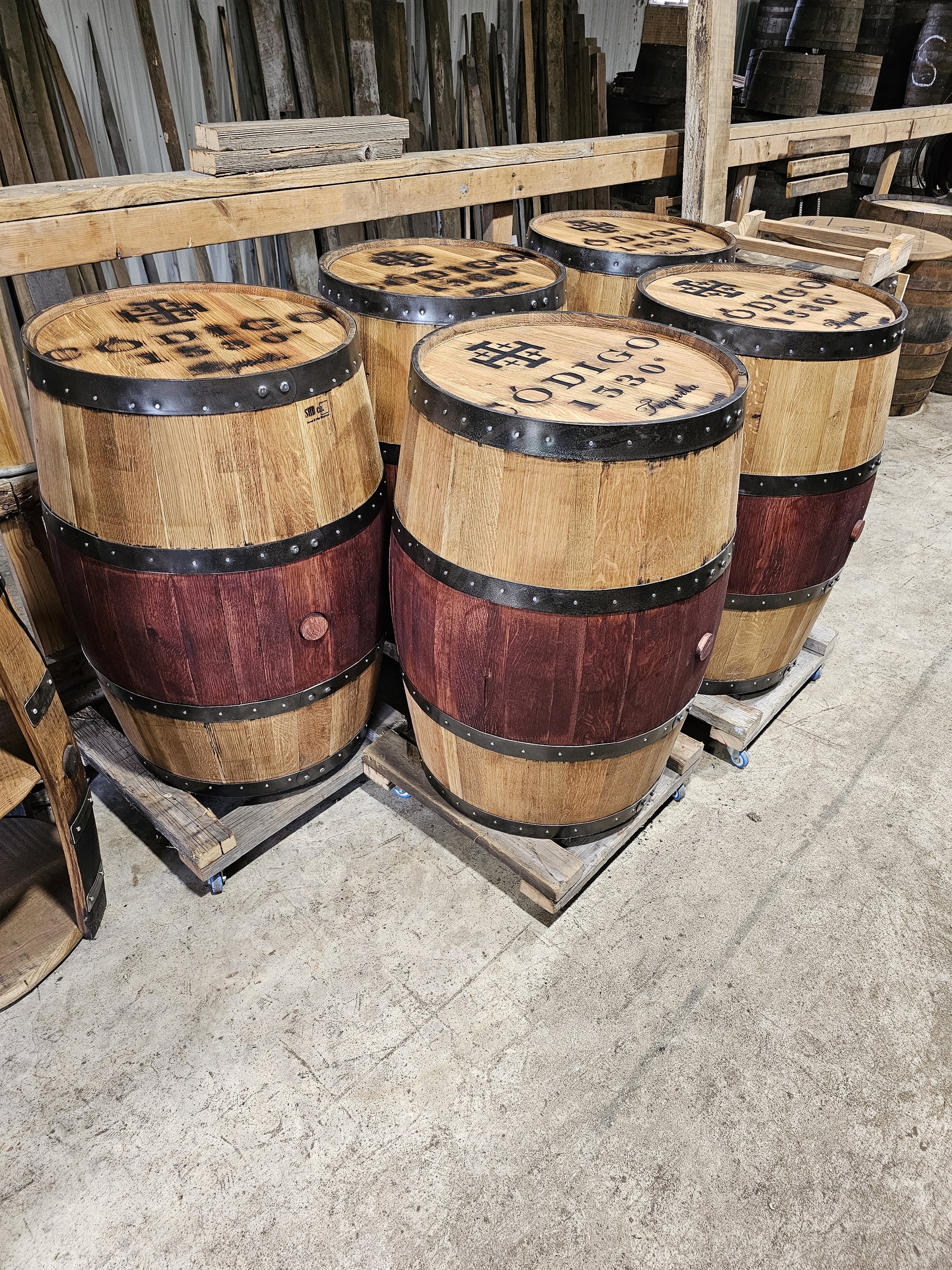 Five completed whiskey-barrel displays with engraved Código 1530 tops and dark red center staves in the SHB workshop.