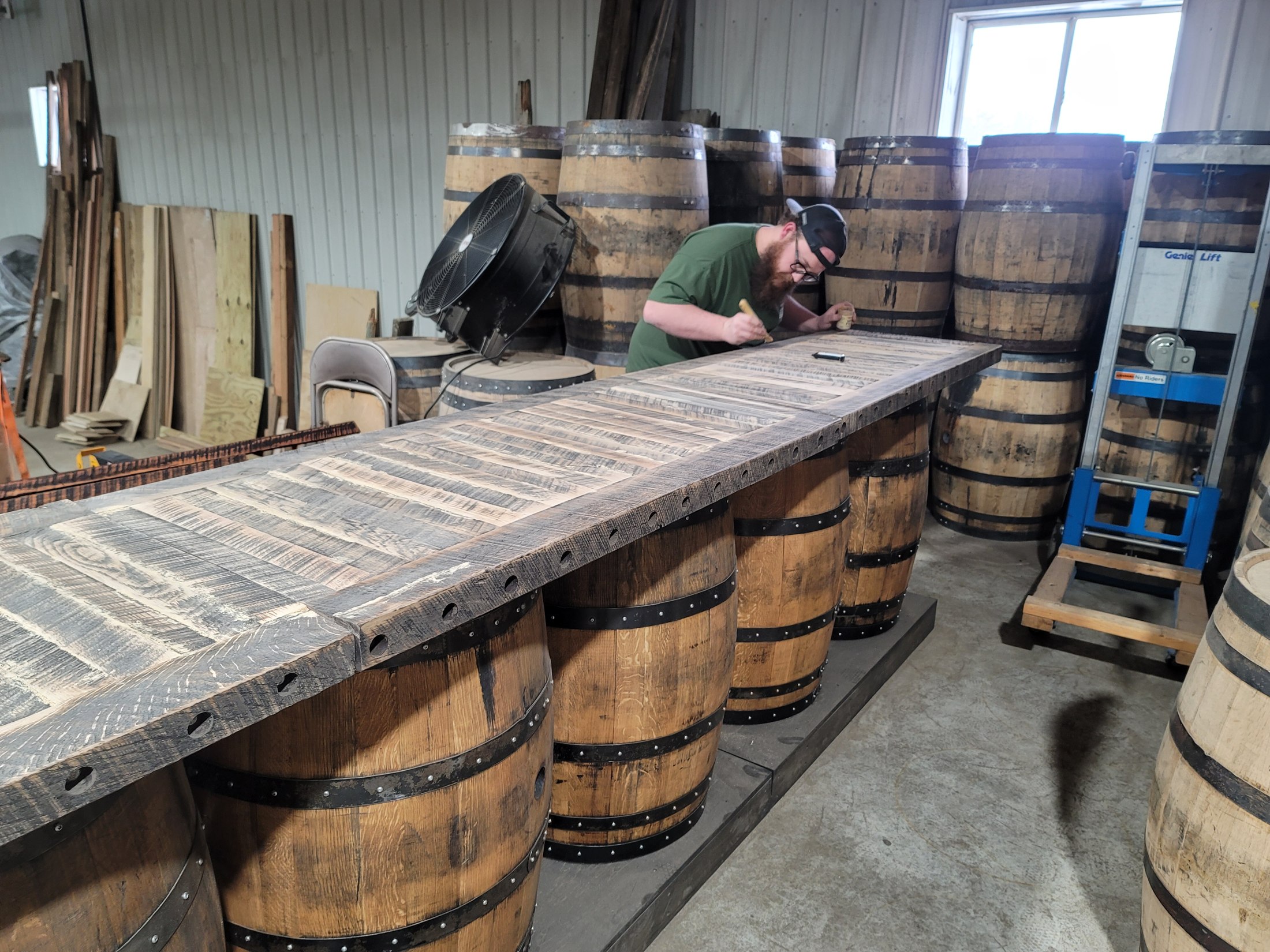 Long segmented wood bar top supported on barrels during shop fabrication.