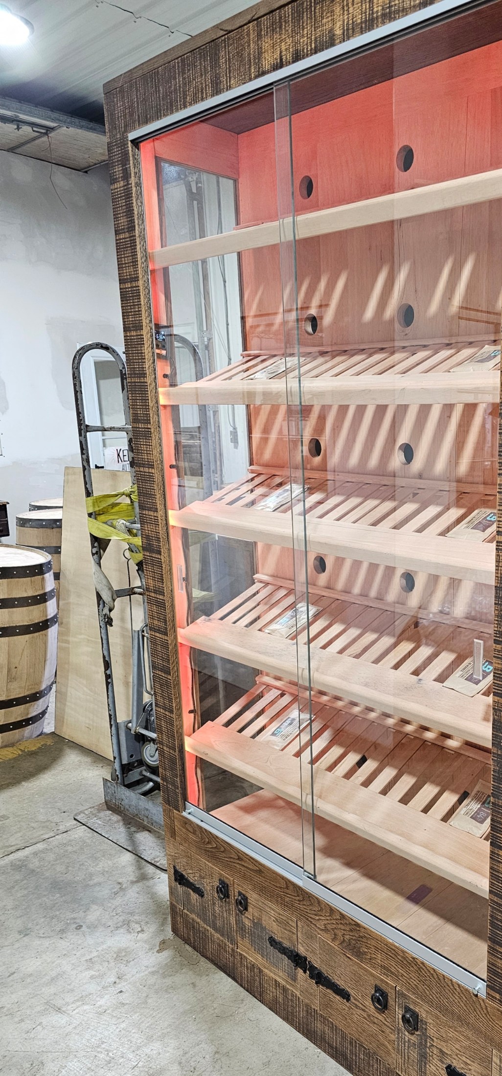 Tall commercial humidor with sliding glass doors, slatted display shelves, a cedar interior and textured wood surround.