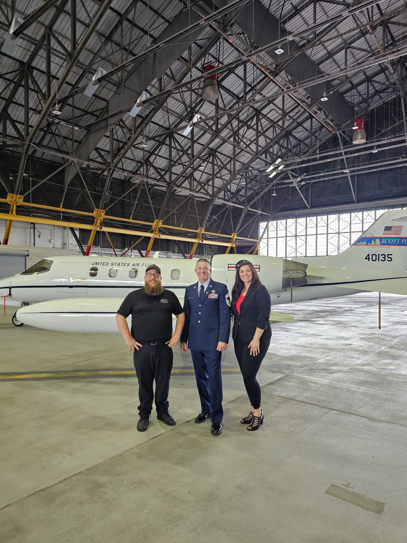 Ryan and Faith with Kris Coats in an aircraft hangar after his Air Force retirement ceremony.