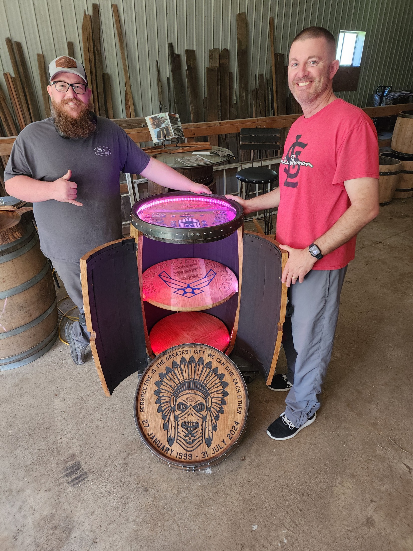 Ryan and Kris Coats beside an illuminated open barrel cabinet and engraved retirement cap in the SHB workshop.