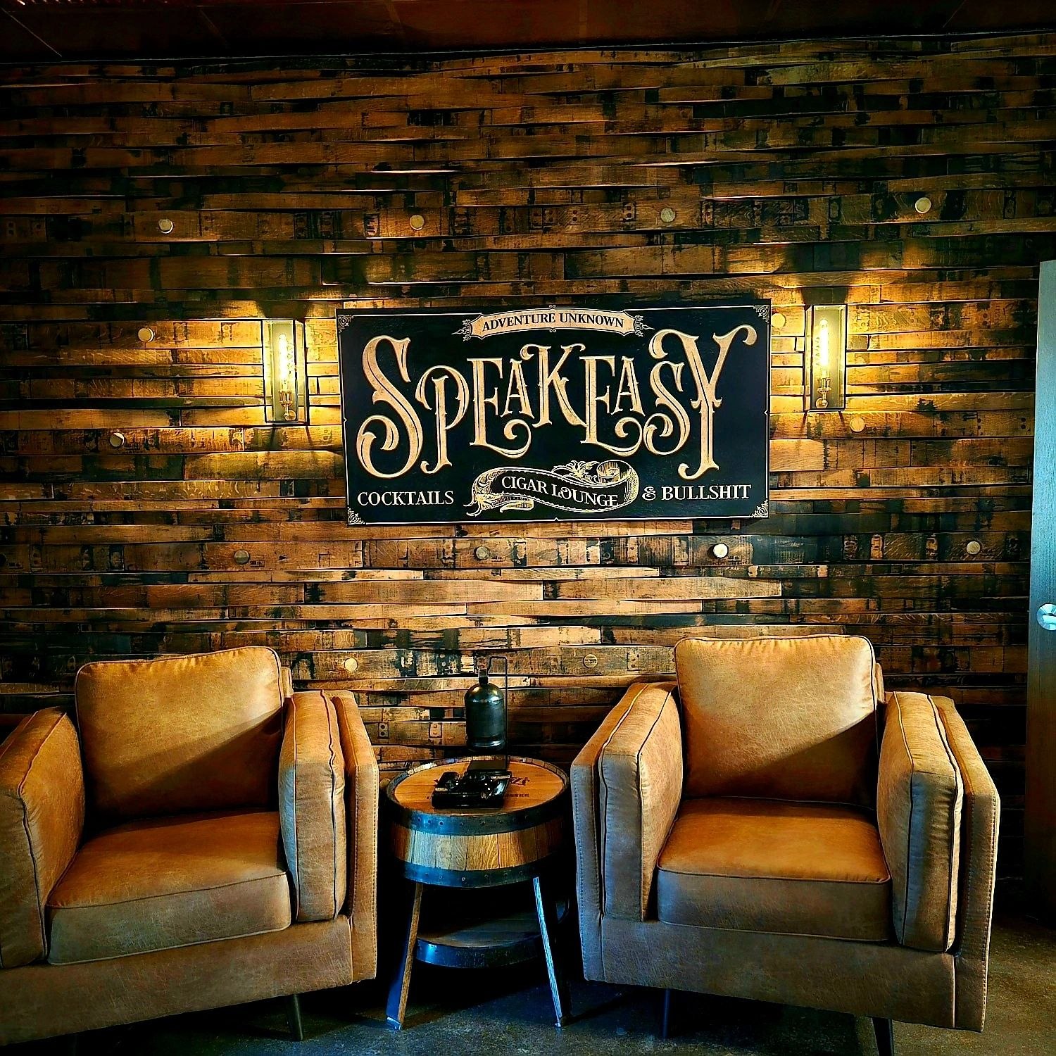 Barrel-stave wall behind the Speakeasy sign and two lounge chairs in Adventure Unknown’s cigar lounge.