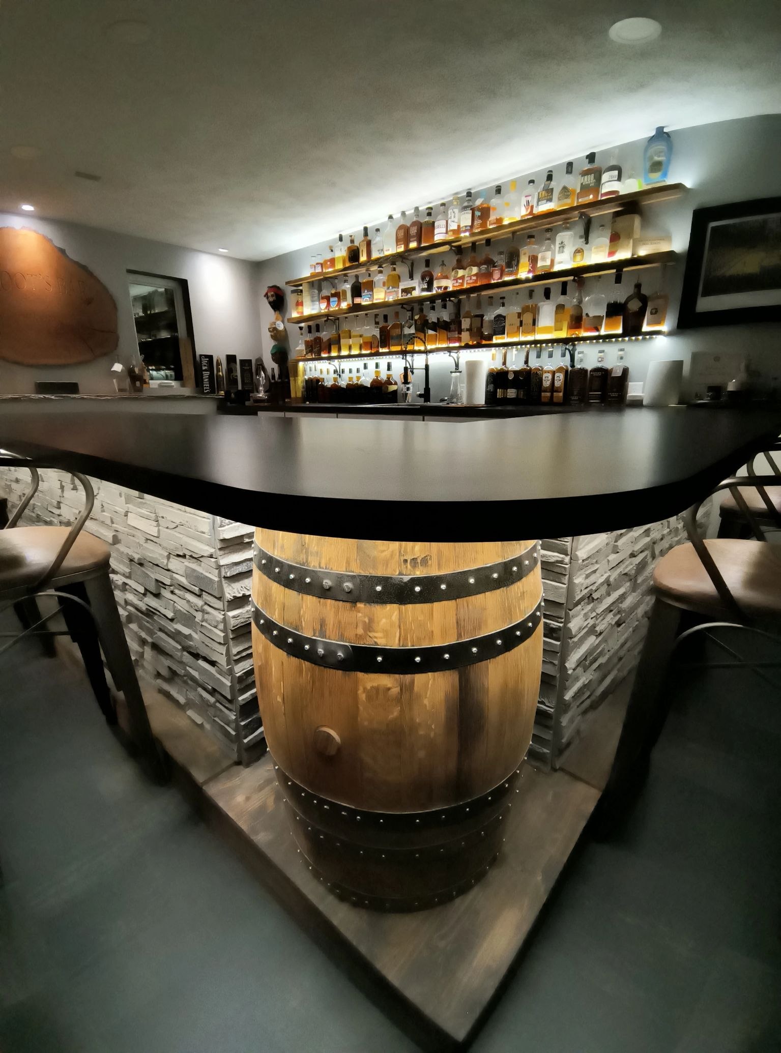The Root Family bar with a dark curved countertop, barrel center detail and illuminated bottle shelves.