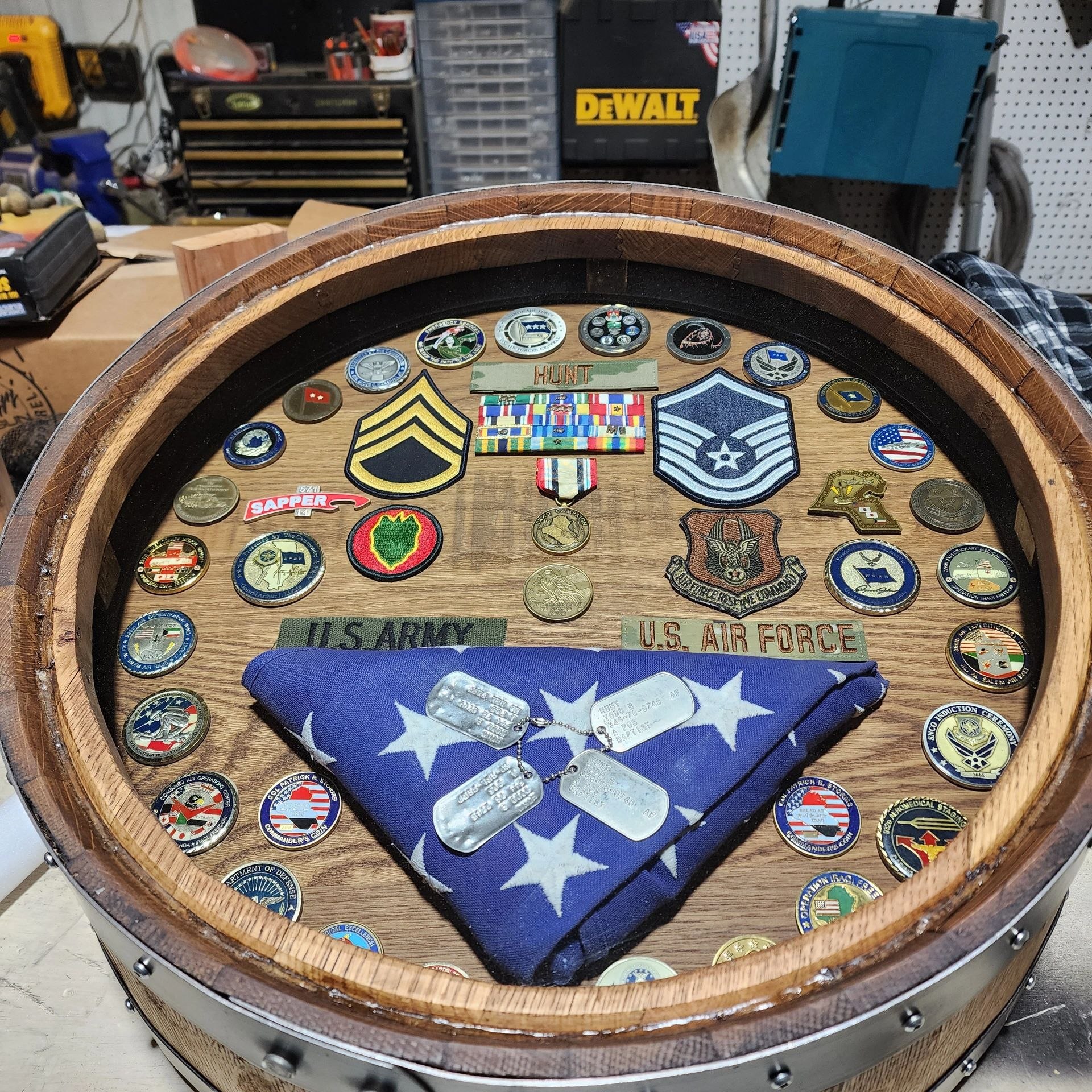 Barrel shadow box in the workshop displaying Army and Air Force insignia and a folded flag.