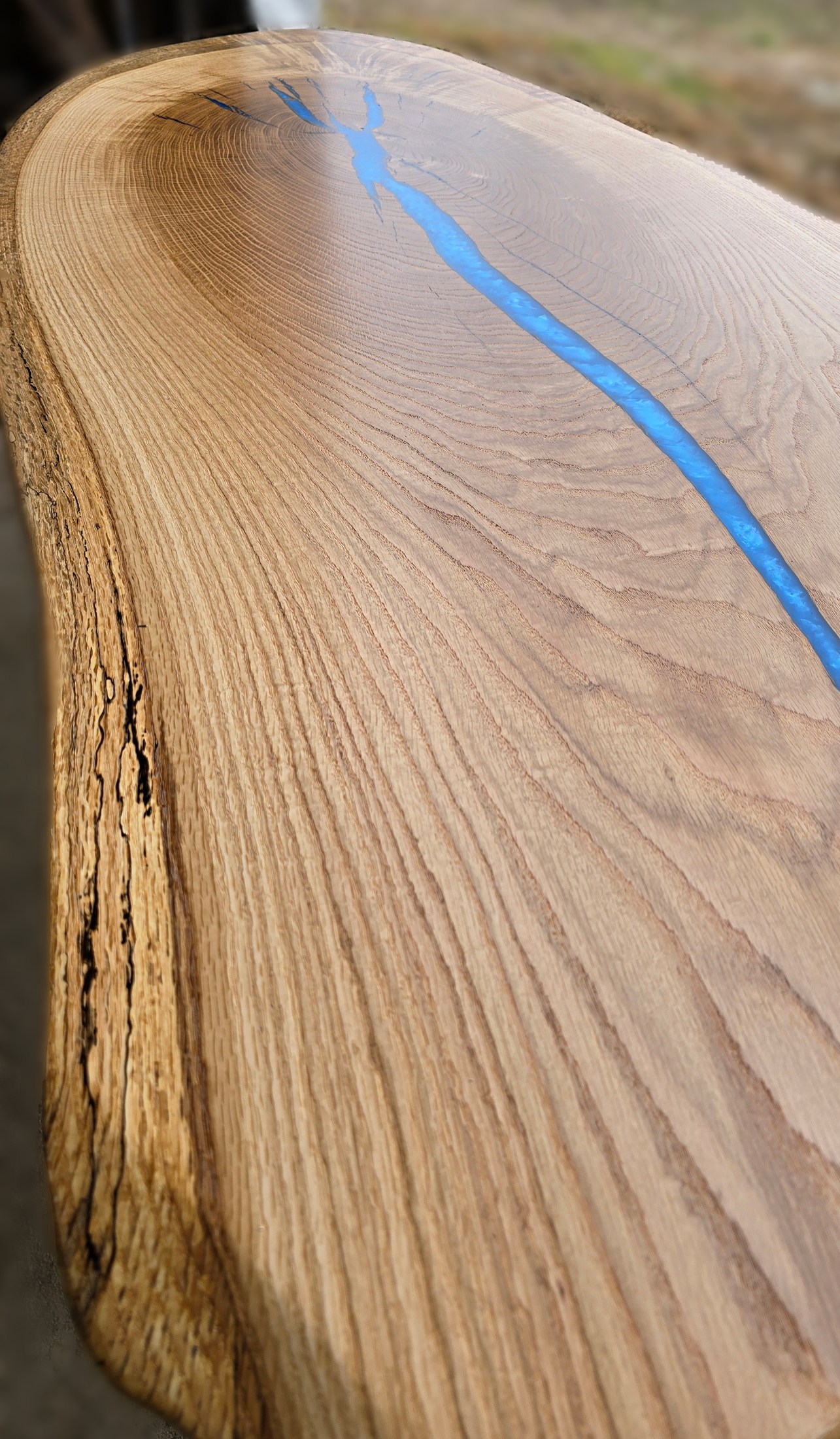 Low angled view along the wood grain and natural edge beside a narrow blue inlay.