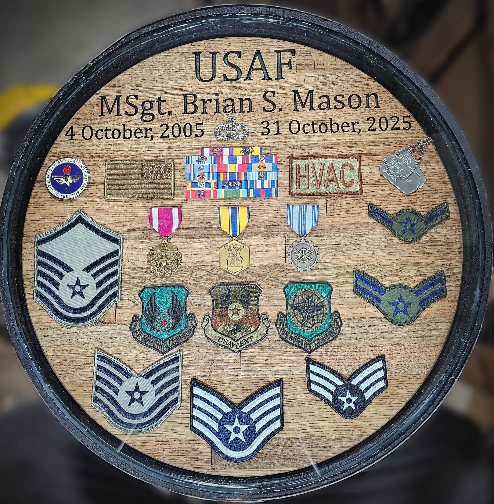 Round Air Force shadow box engraved USAF MSgt. Brian S. Mason, containing service ribbons, rank insignia, coins and badges under glass.