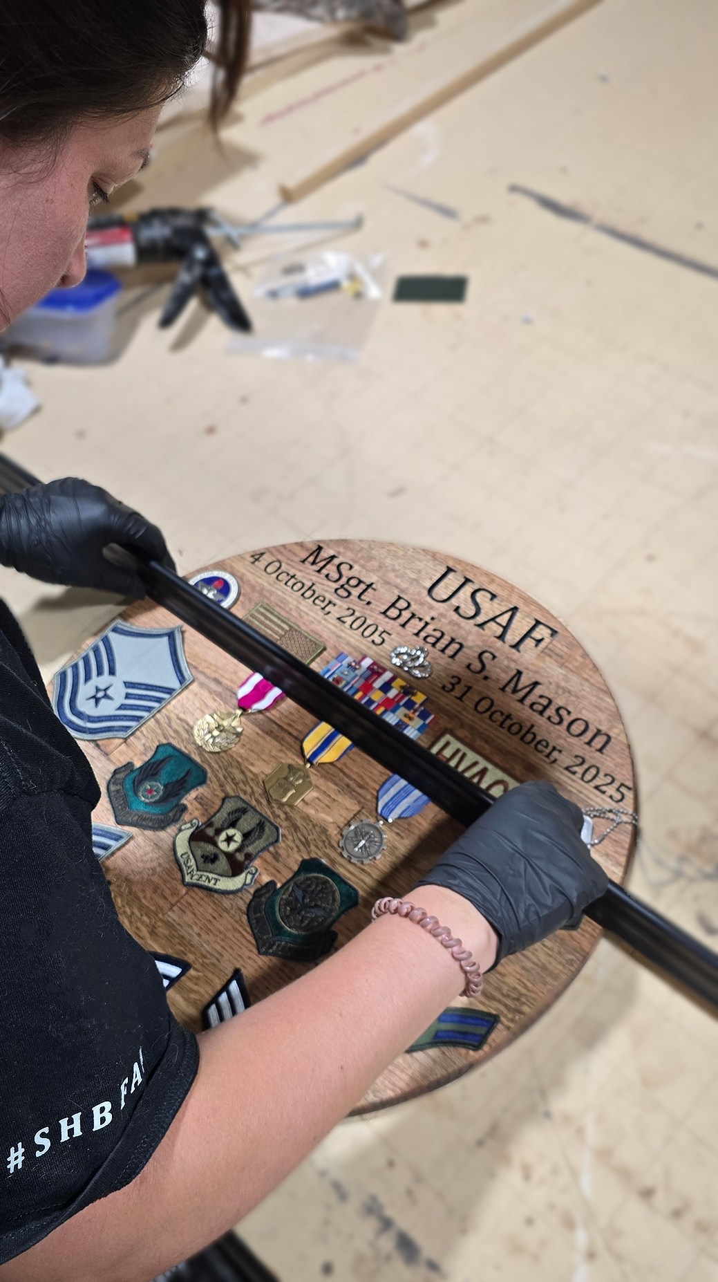 Hands arranging ribbons and insignia on the engraved backing of Brian Mason’s shadow box at the workshop bench.