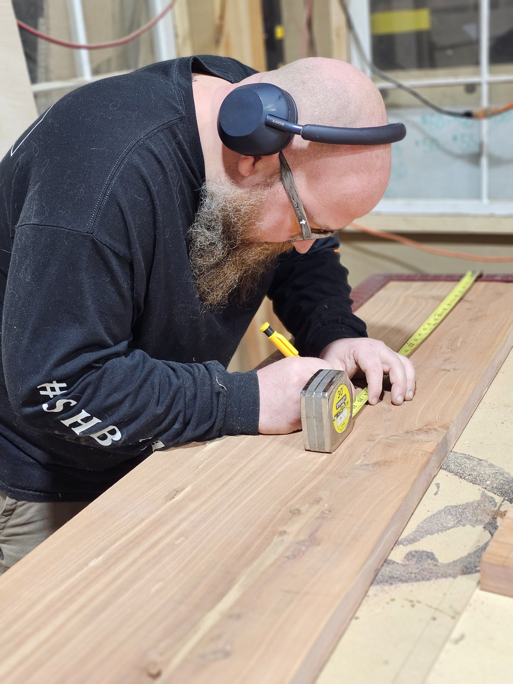 Craftsman in an SHB shirt measuring wood at the workbench.