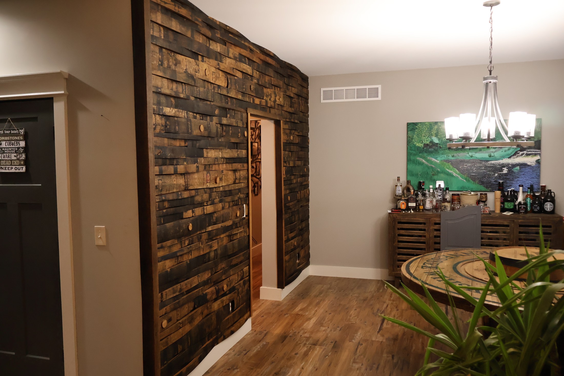 Wide room view of the barrel-stave wall around a doorway beside a dining area and drinks cabinet.