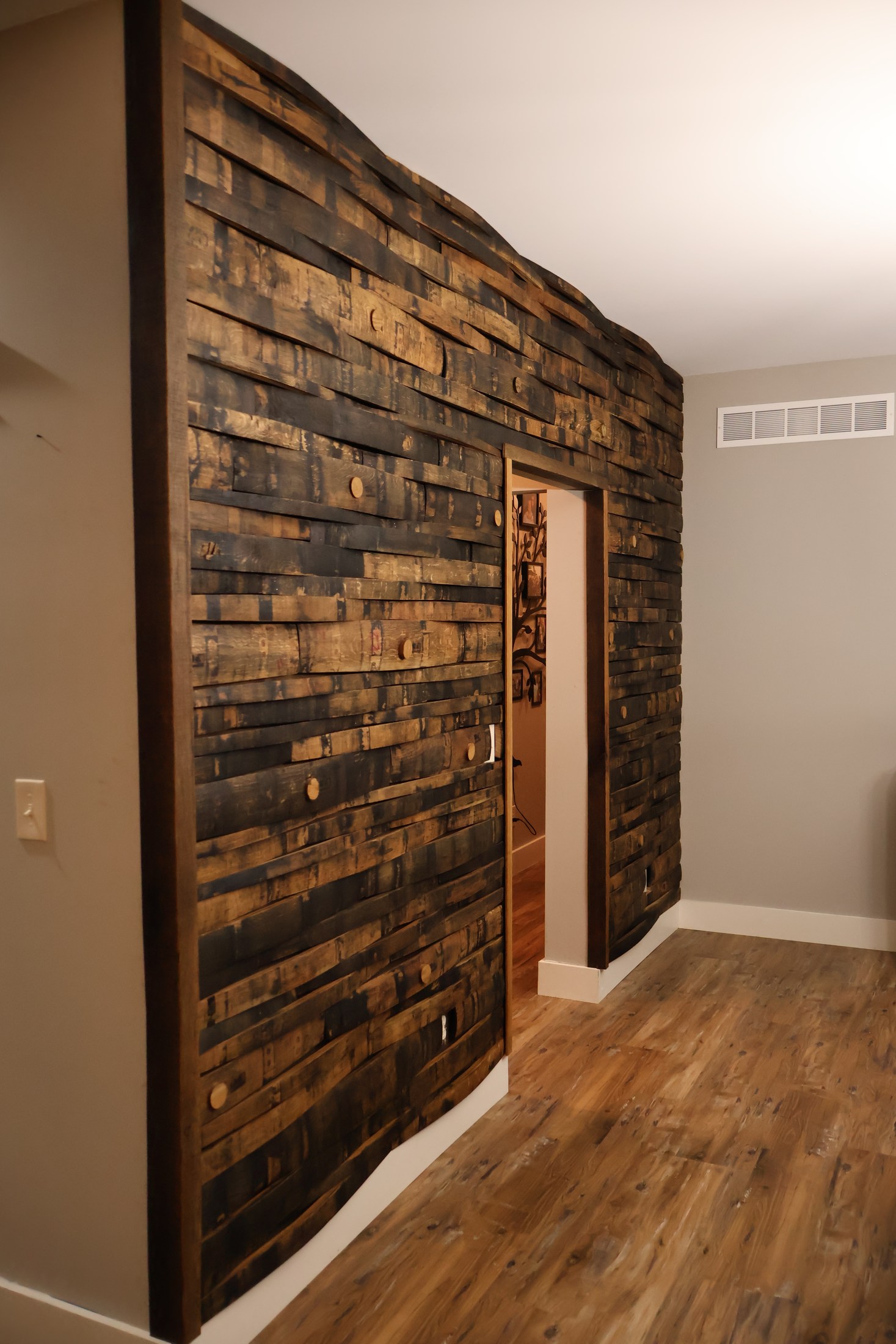A wall clad in staggered barrel staves frames a doorway in a Moscow Mills home.