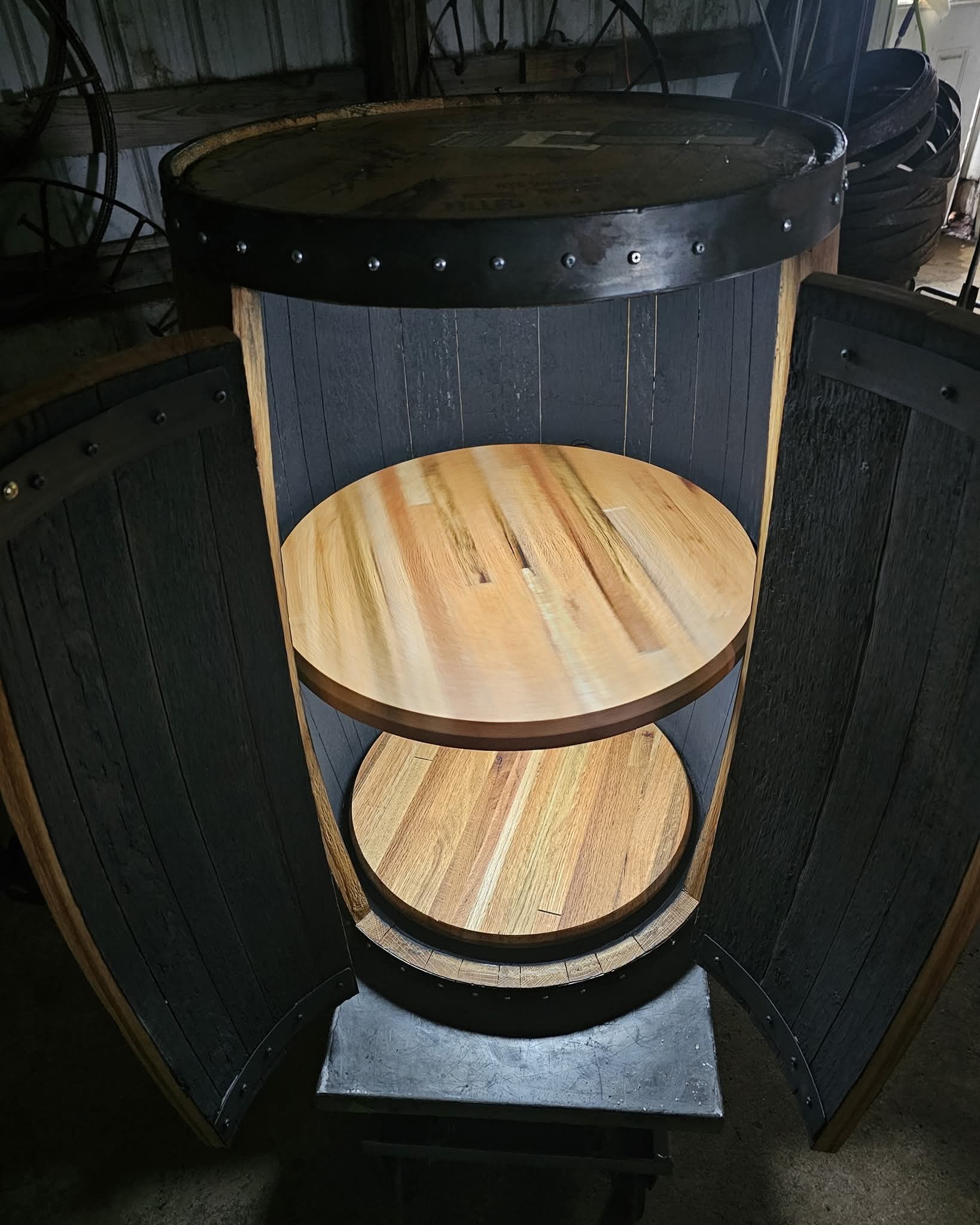 The barrel cabinet with both doors open, showing two round wood shelves against the dark interior.