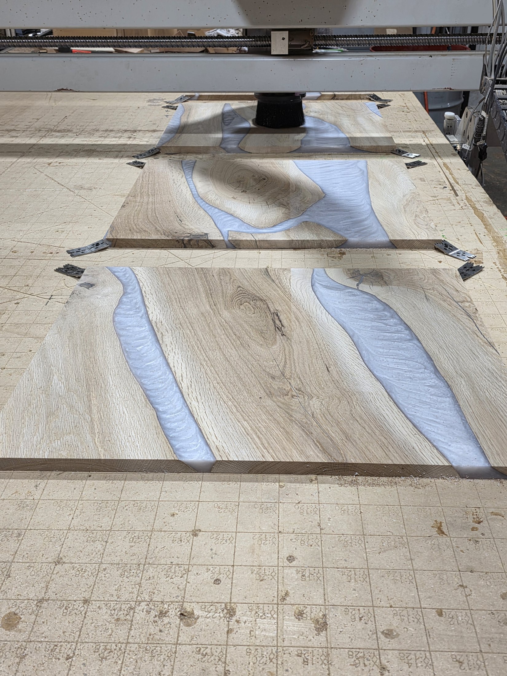 Wood-and-white-epoxy door panel secured on the CNC bed during surfacing.