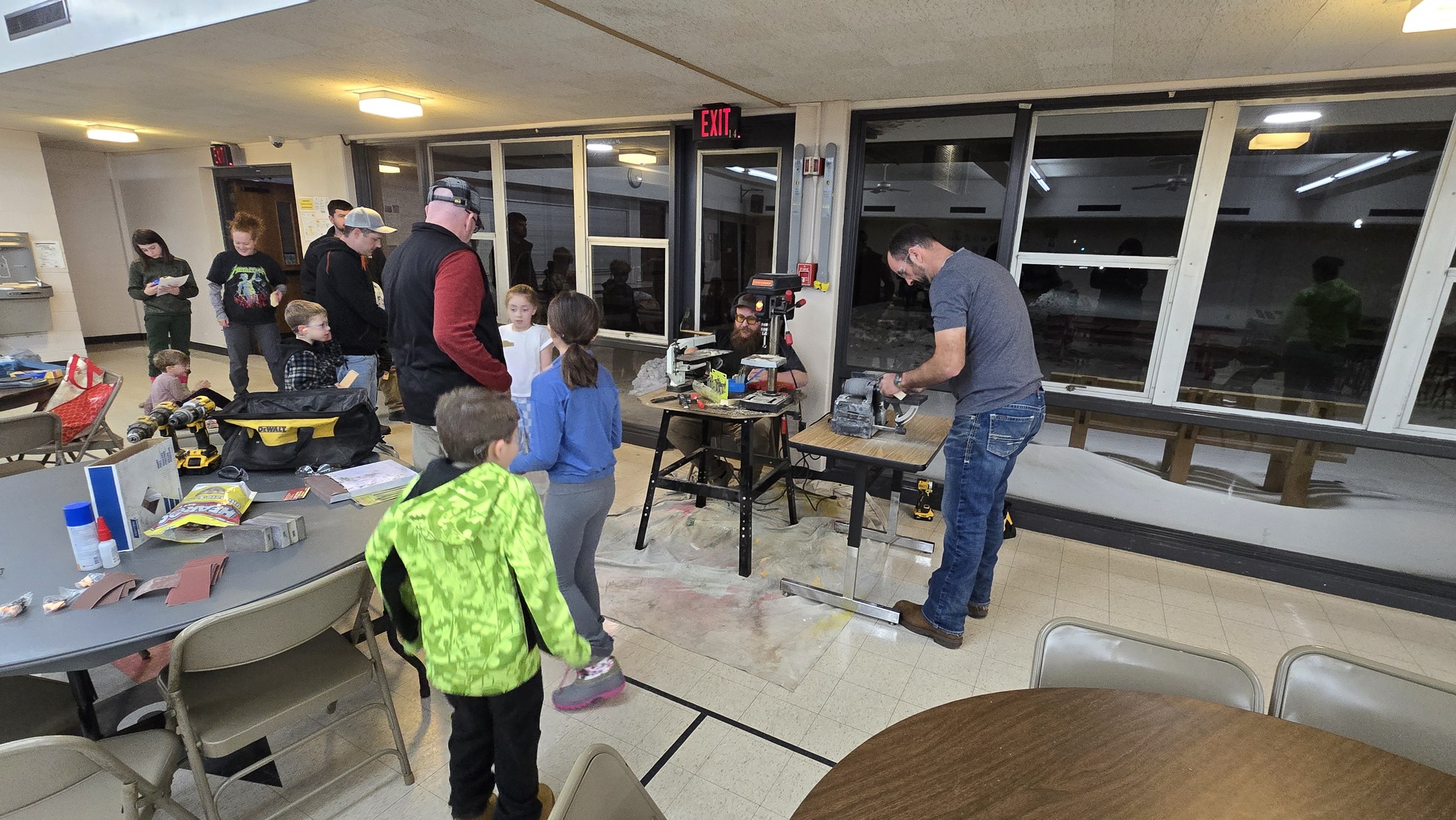 Two volunteer workstations with woodworking tools, car blanks, Scouts and adults at the Pinewood Derby event.