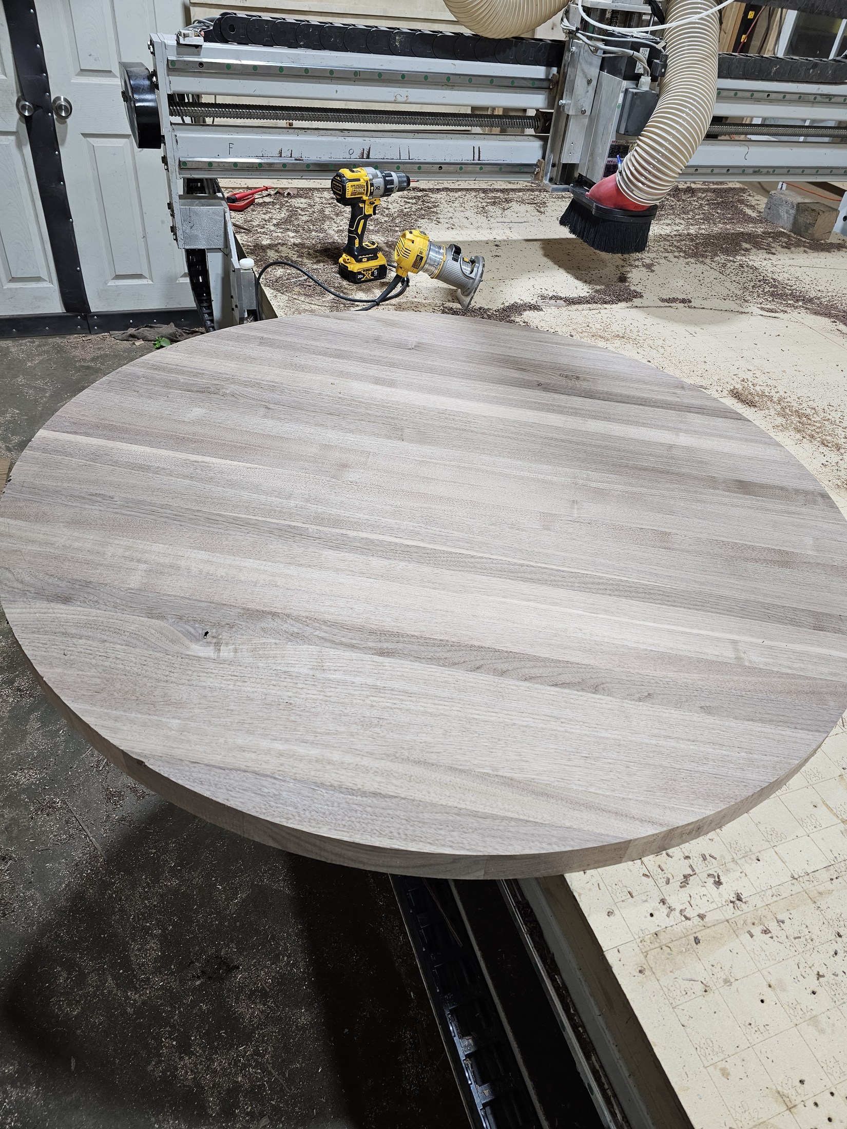 Round wood tabletop beneath the CNC spindle with the machine gantry above it.