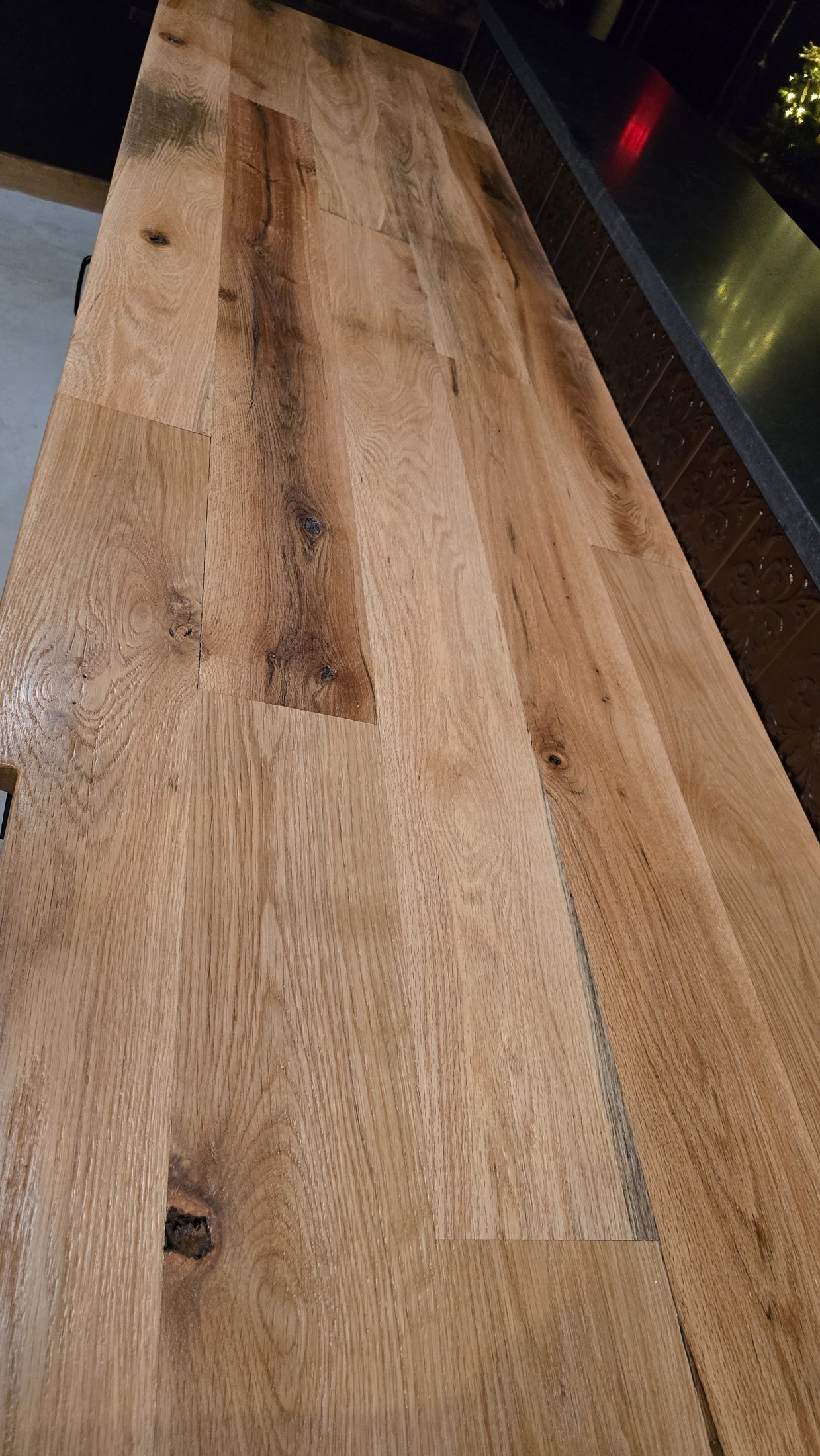 Close view of a broad wooden surface beside the Rustic Roots bar, showing grain, knots and joined boards.