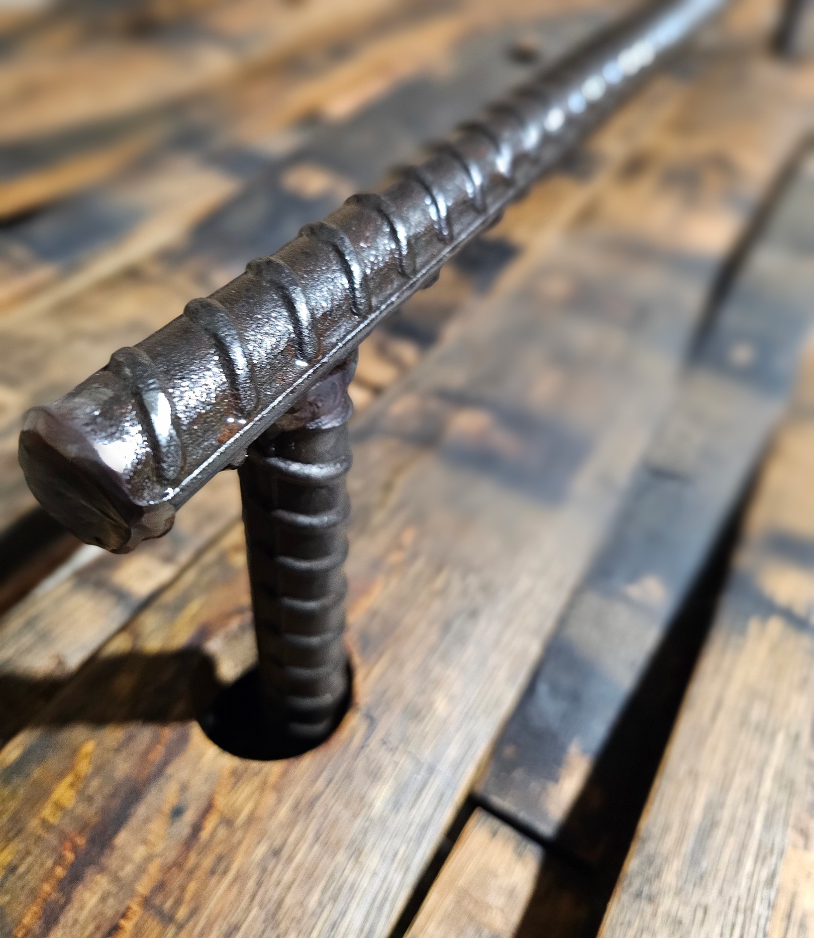 Close view of a welded rebar footrail support passing through a round bung hole in a barrel stave on the workshop bench.