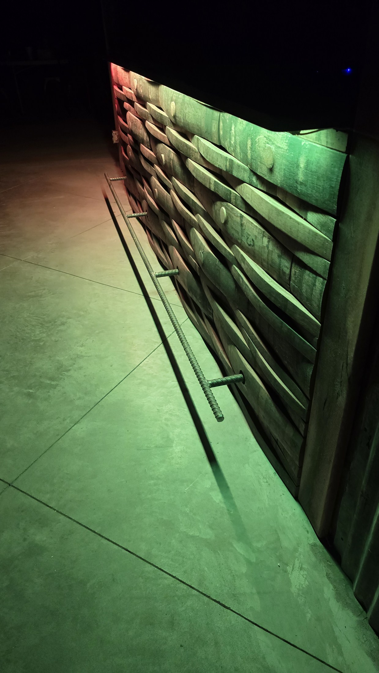 Rebar footrail follows a barrel-stave bar front at Rustic Roots, with supports passing through the original bung holes under colored lighting.