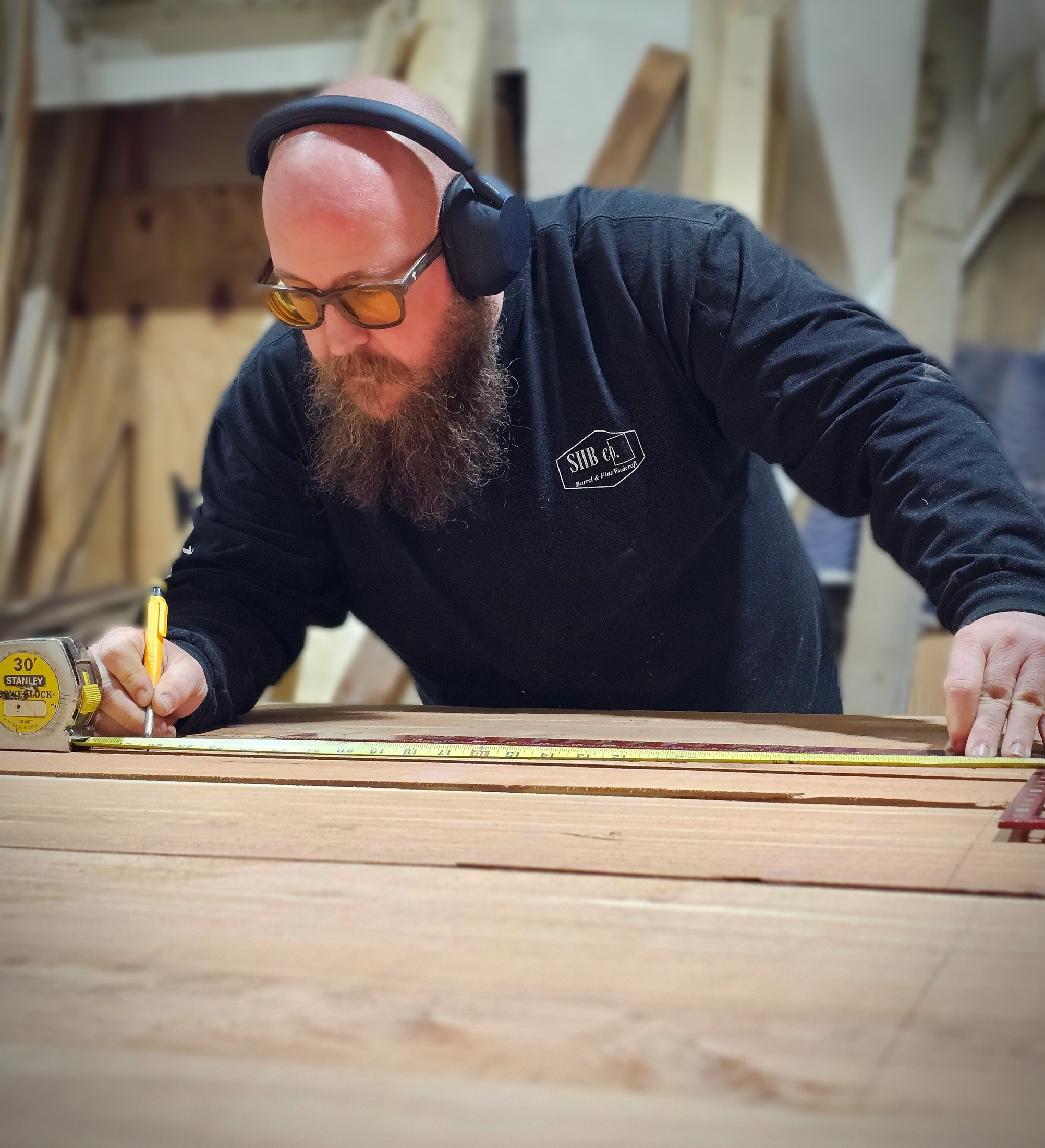Ryan wearing hearing protection while marking a wood panel with a pencil and measuring tape.