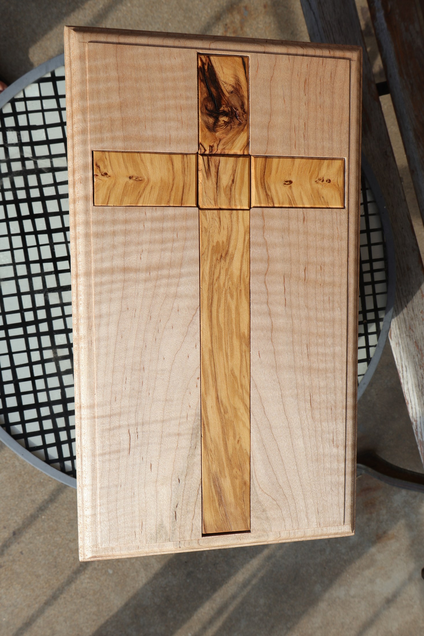 Top view of a wood cross set into the pale figured lid of the memorial box.