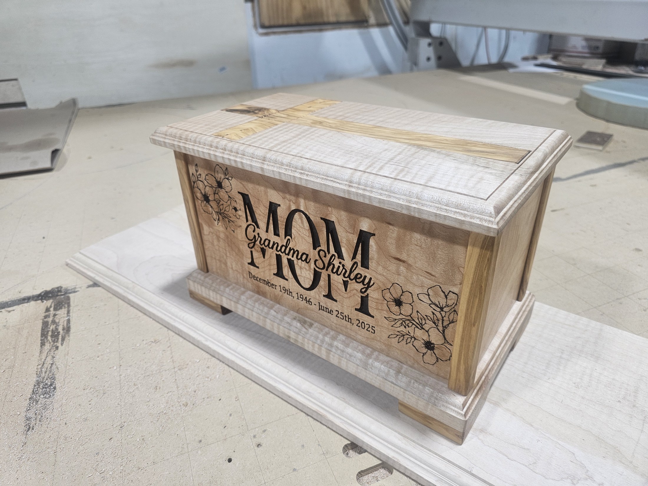 Completed memorial box resting on the workshop bench, showing the engraved front and cross in the lid.