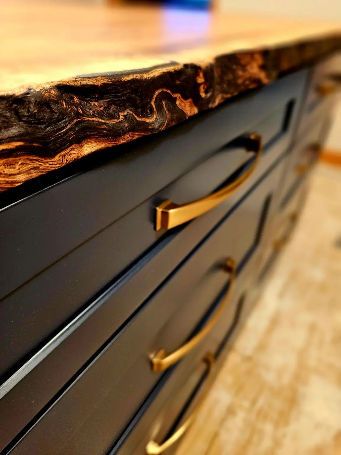 Close view of the irregular live edge above navy drawers and brushed brass handles.