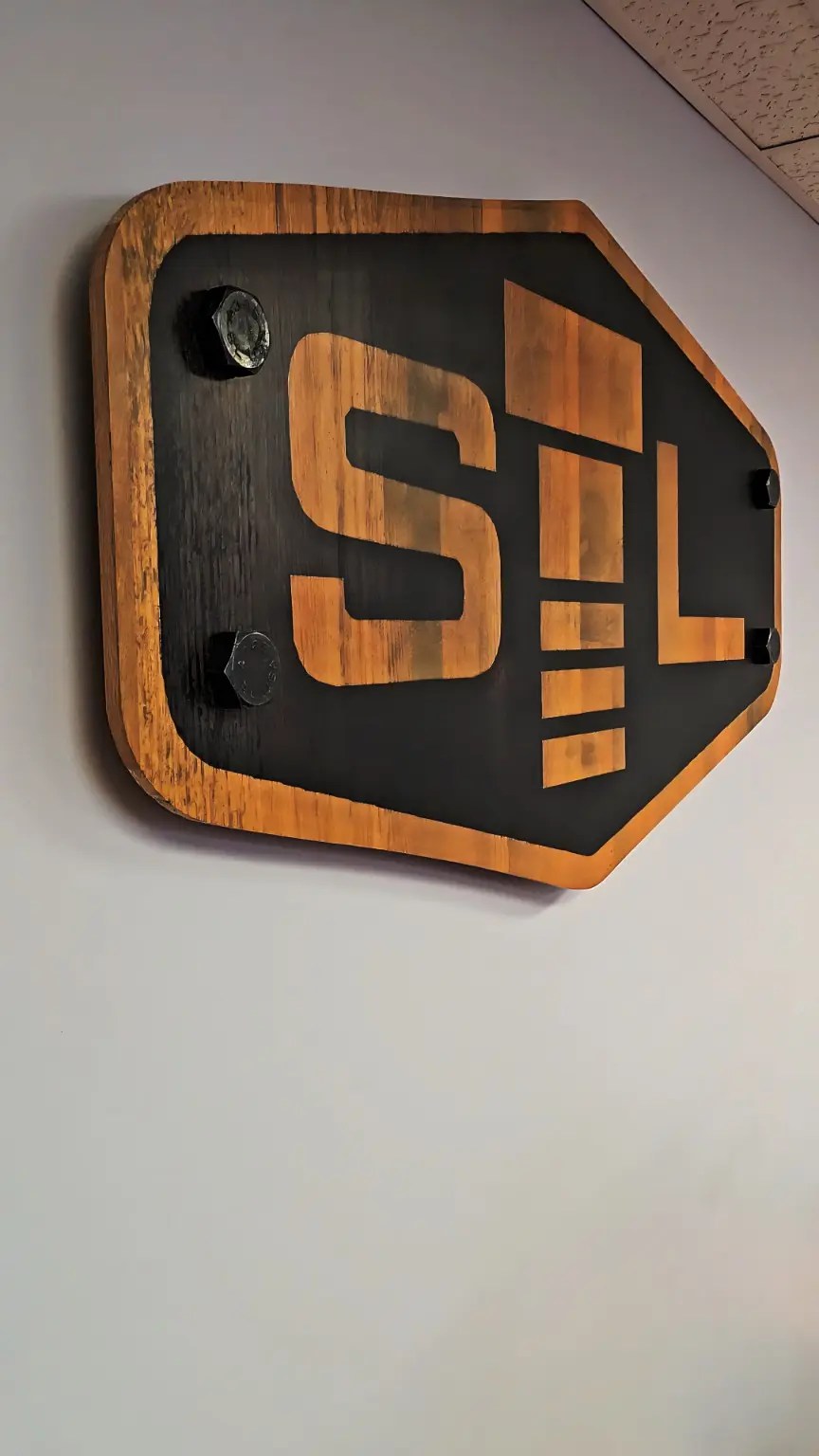 Dimensional STL wood sign with large bolt heads mounted on the gray meeting-room wall.
